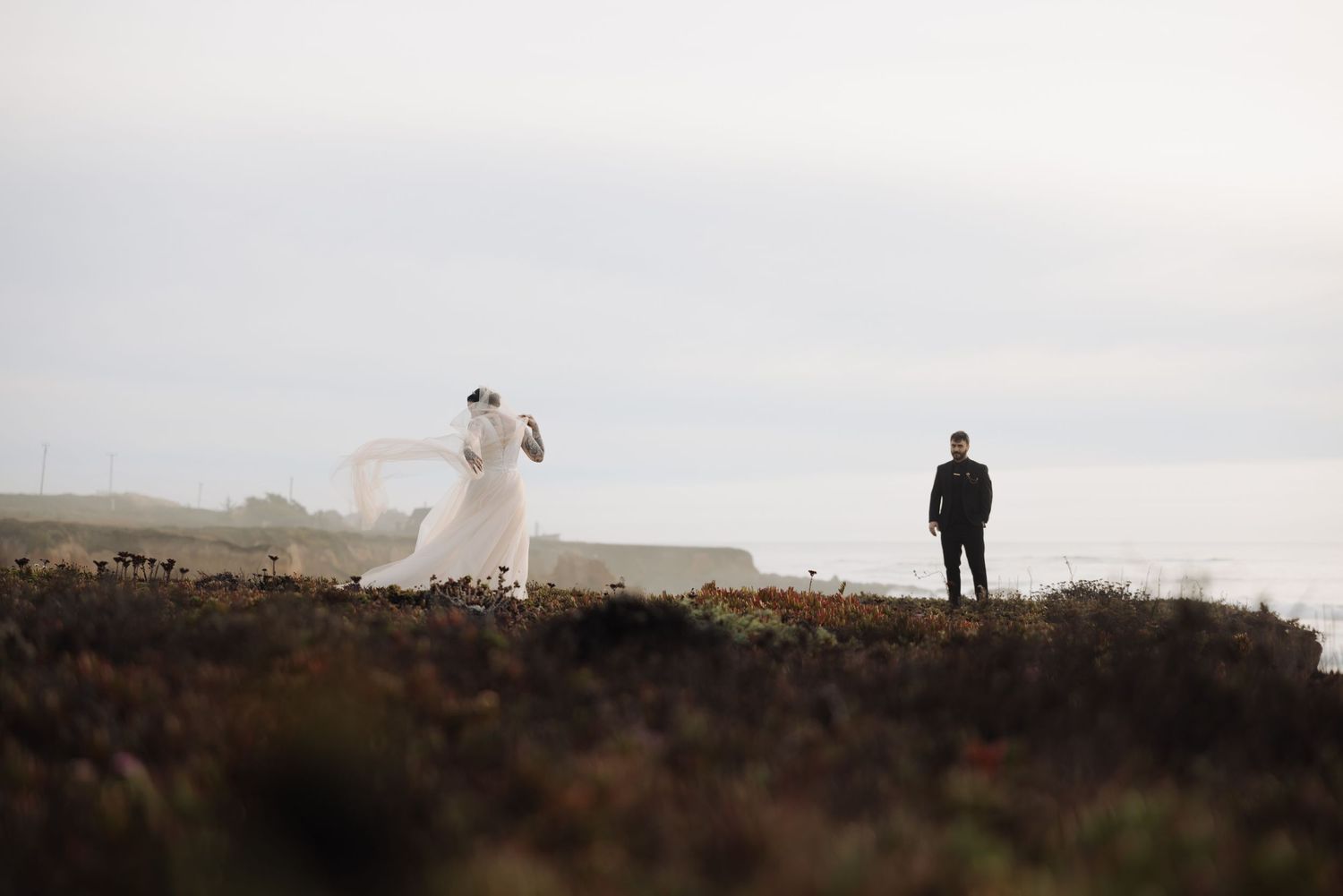 Distant figures on windswept coastal cliffs with ocean waves below.