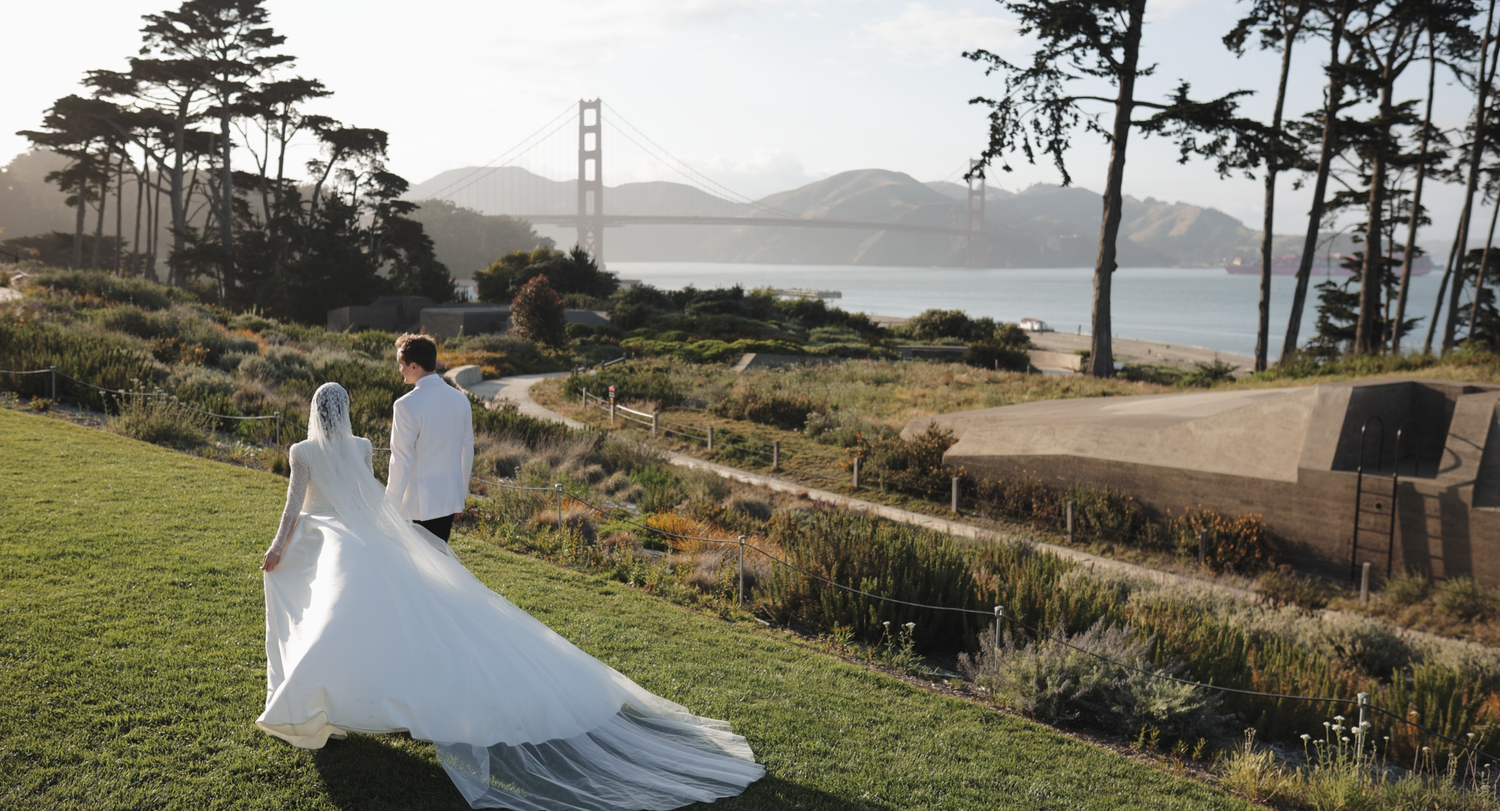 Bride and groom walk hand-in-hand at Presidio with Golden Gate Bridge backdrop on their wedding day.