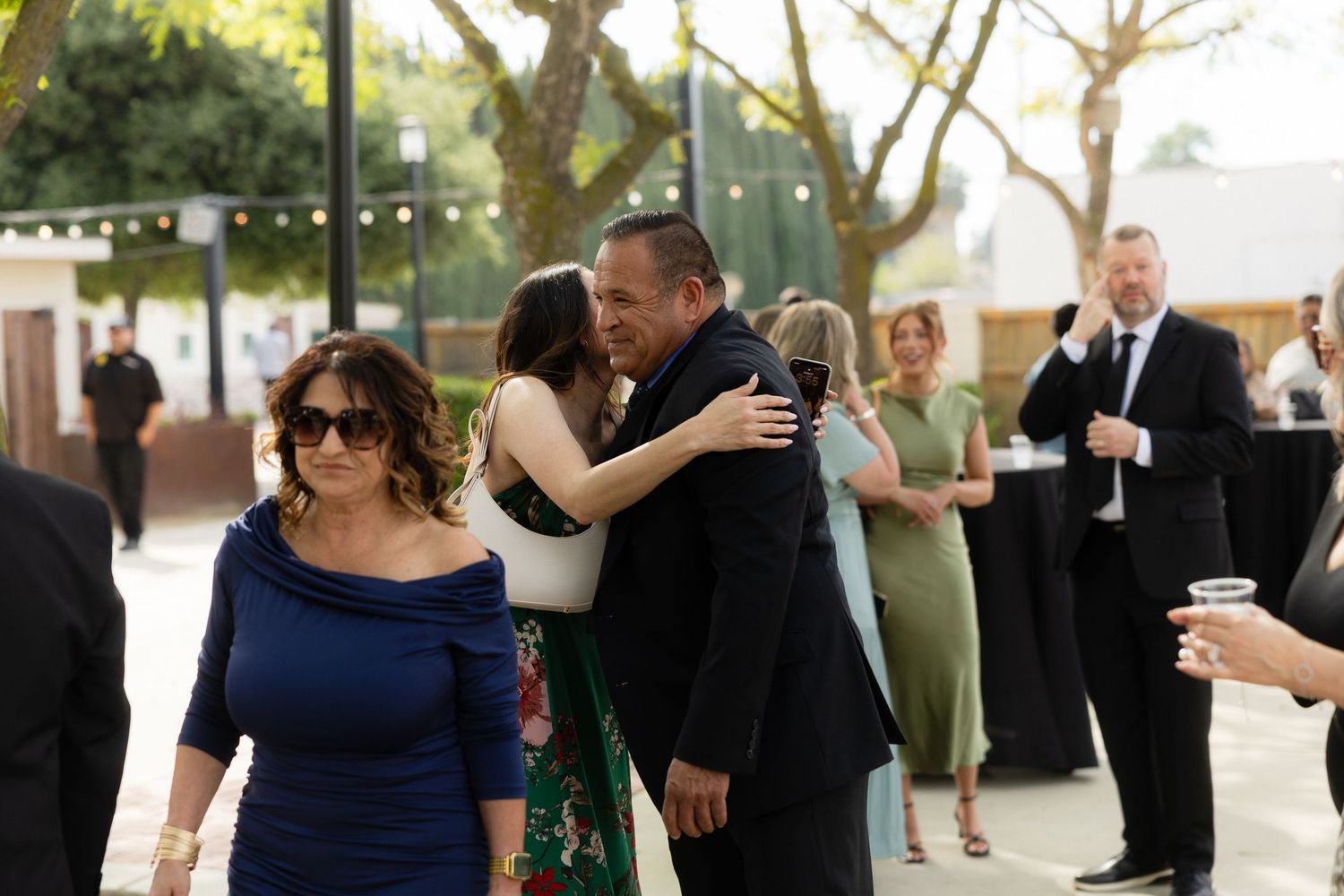 Guests embracing and socializing at an outdoor wedding reception venue with string lights.