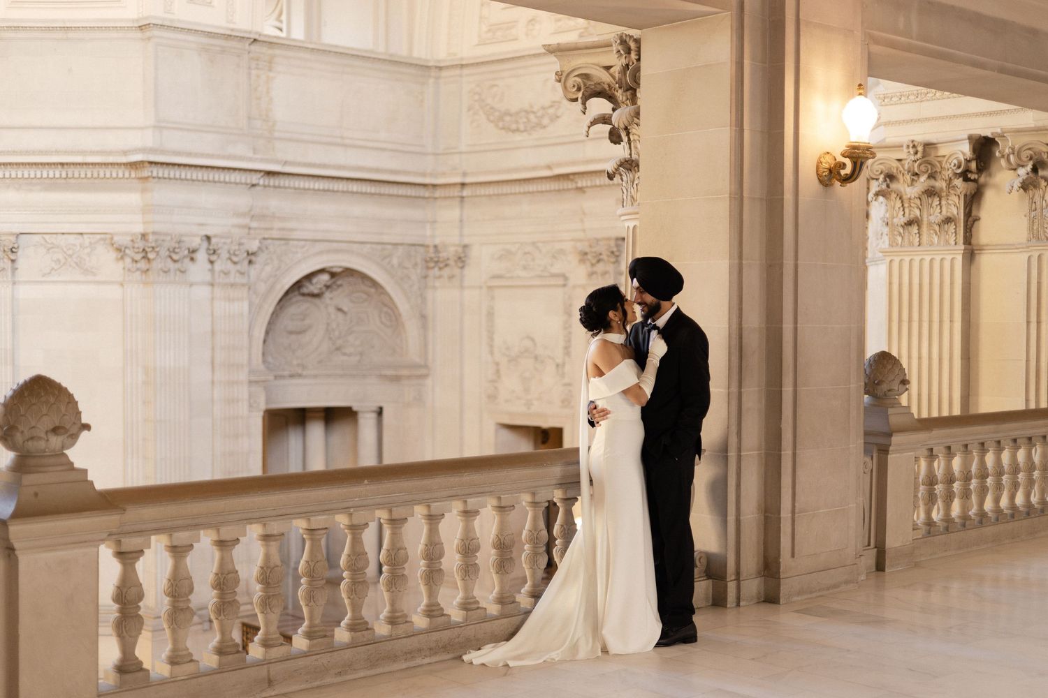 A romantic moment captured on an elegant marble staircase with ornate architectural details and warm lighting.