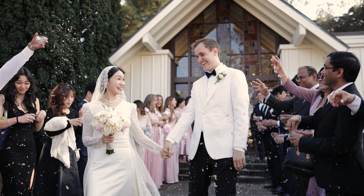 Wedding celebration outside a white chapel with guests throwing confetti in celebration.