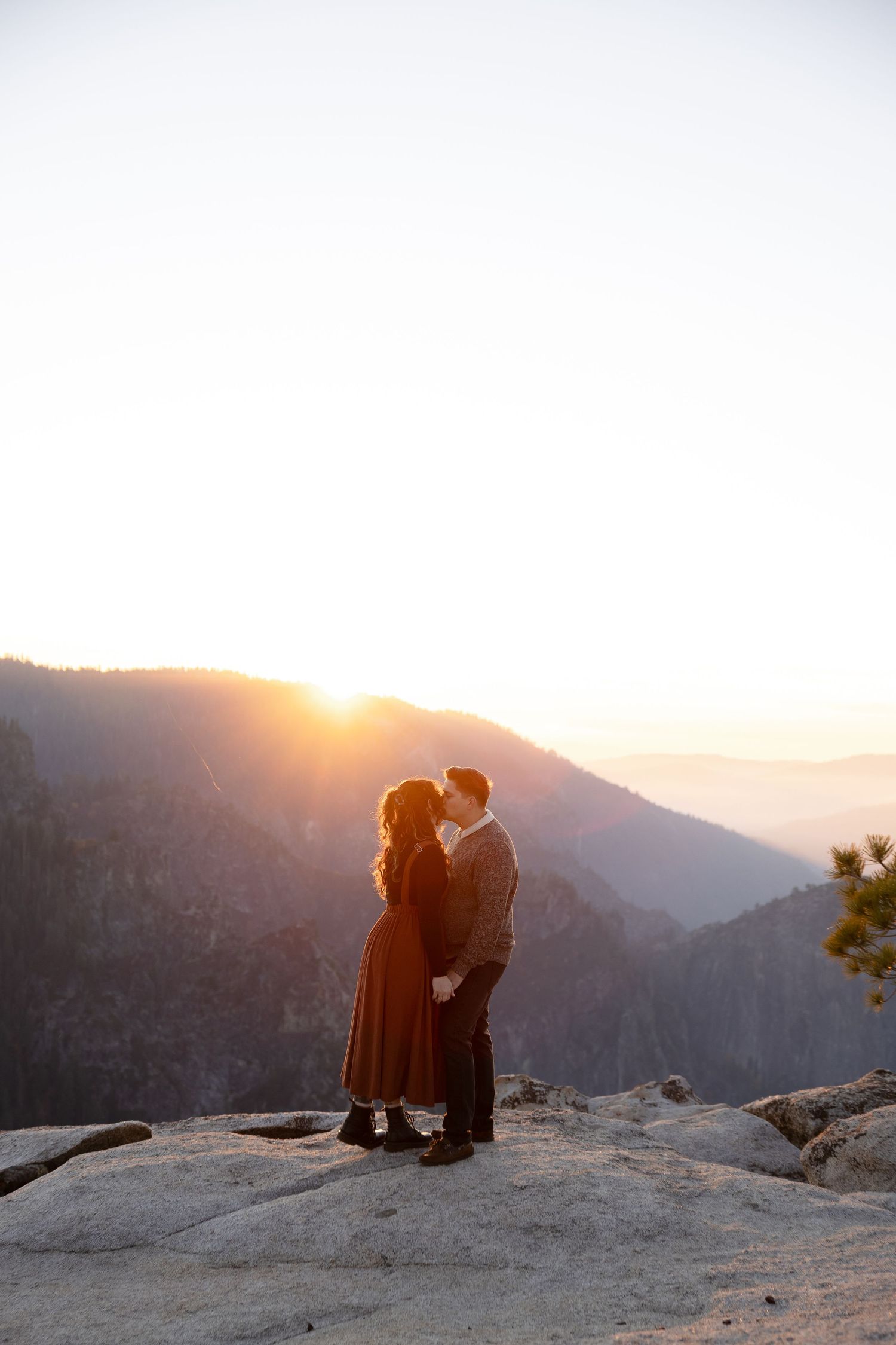 A romantic sunset moment unfolds between two people on a mountain peak.