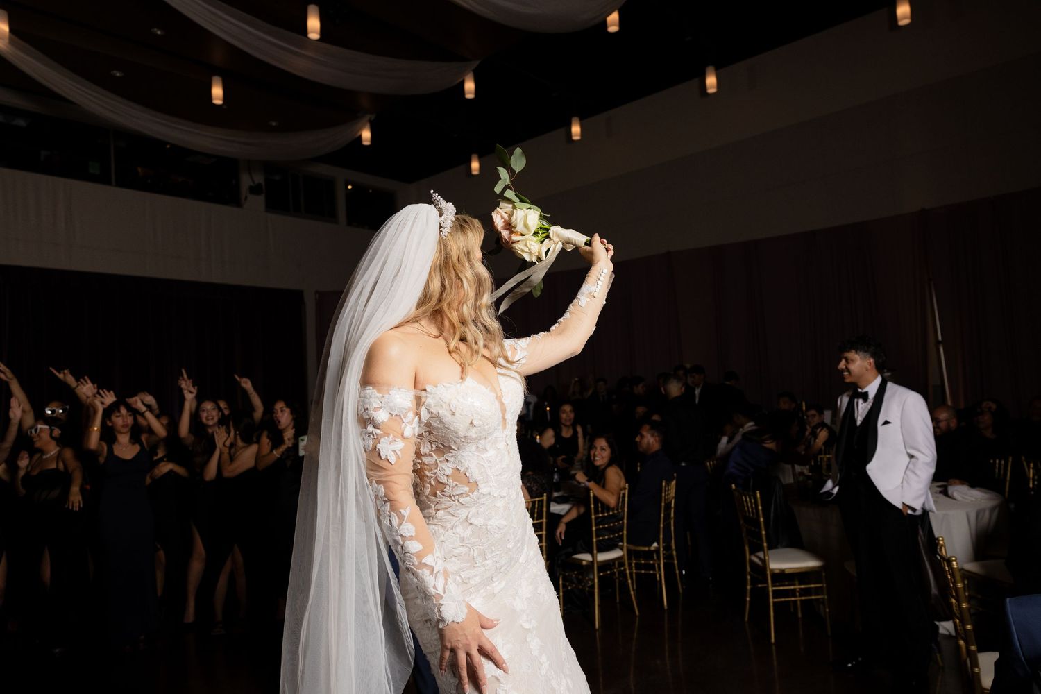Wedding celebration with guests dancing under soft lighting and decorative ceiling fixtures.