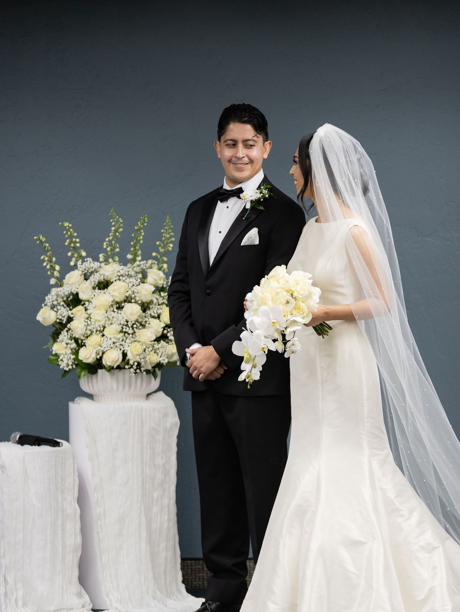 Wedding portrait session with white floral arrangements and elegant bridal couple against grey backdrop.
