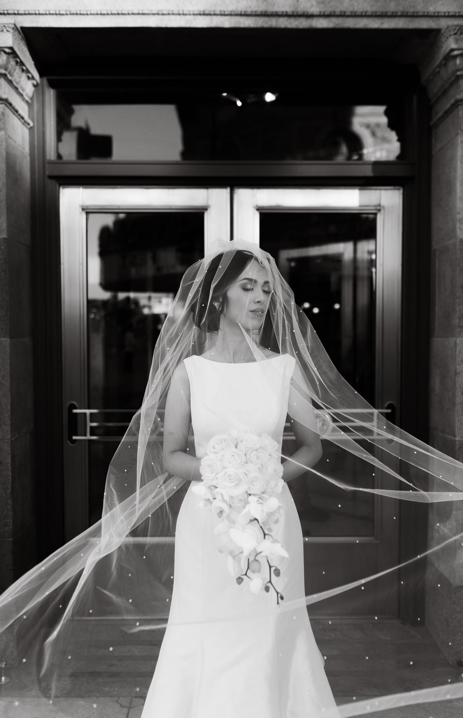 Black and white portrait of a bride with a long flowing veil in an elegant white dress.
