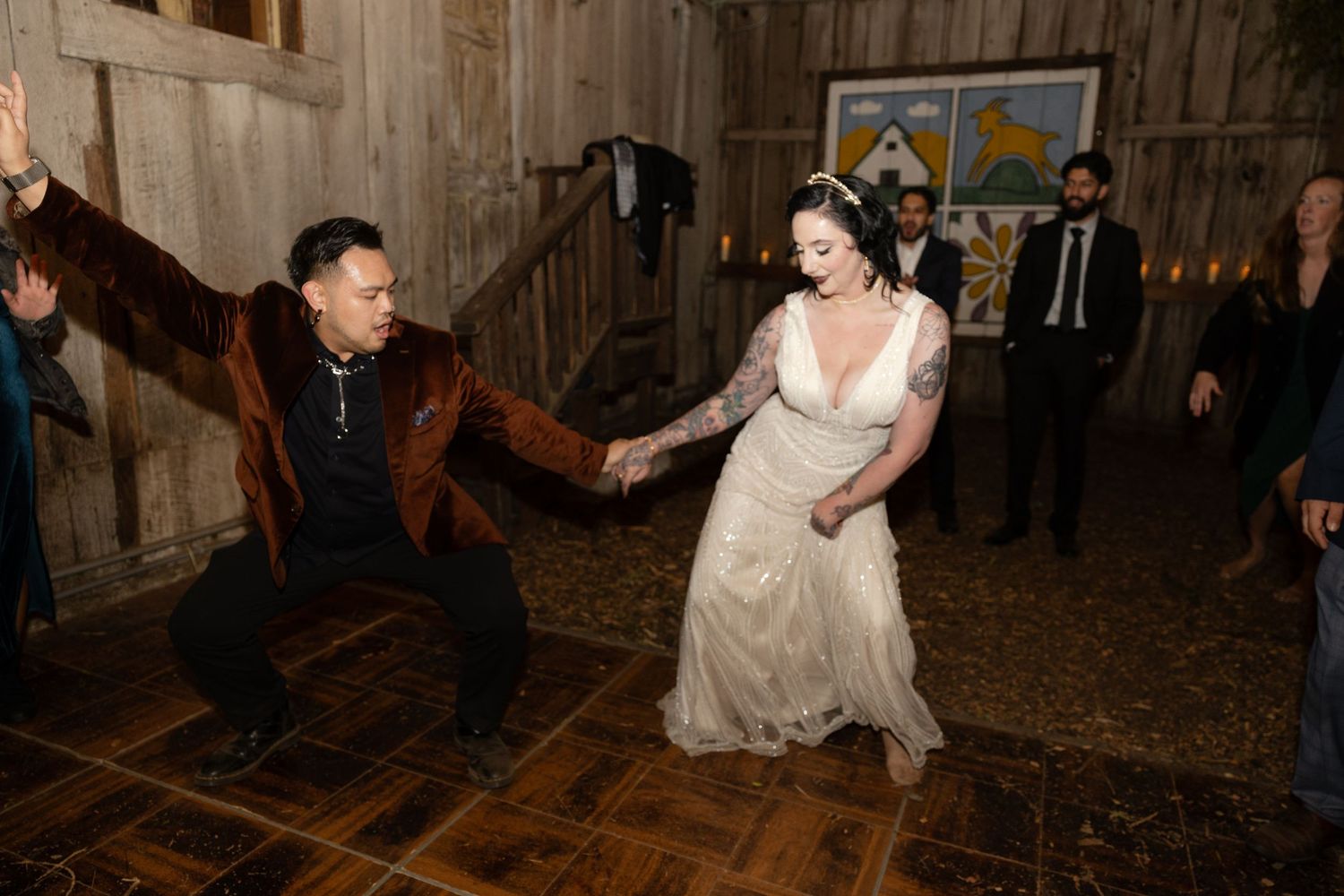Wedding party members dancing enthusiastically at a rustic barn reception.