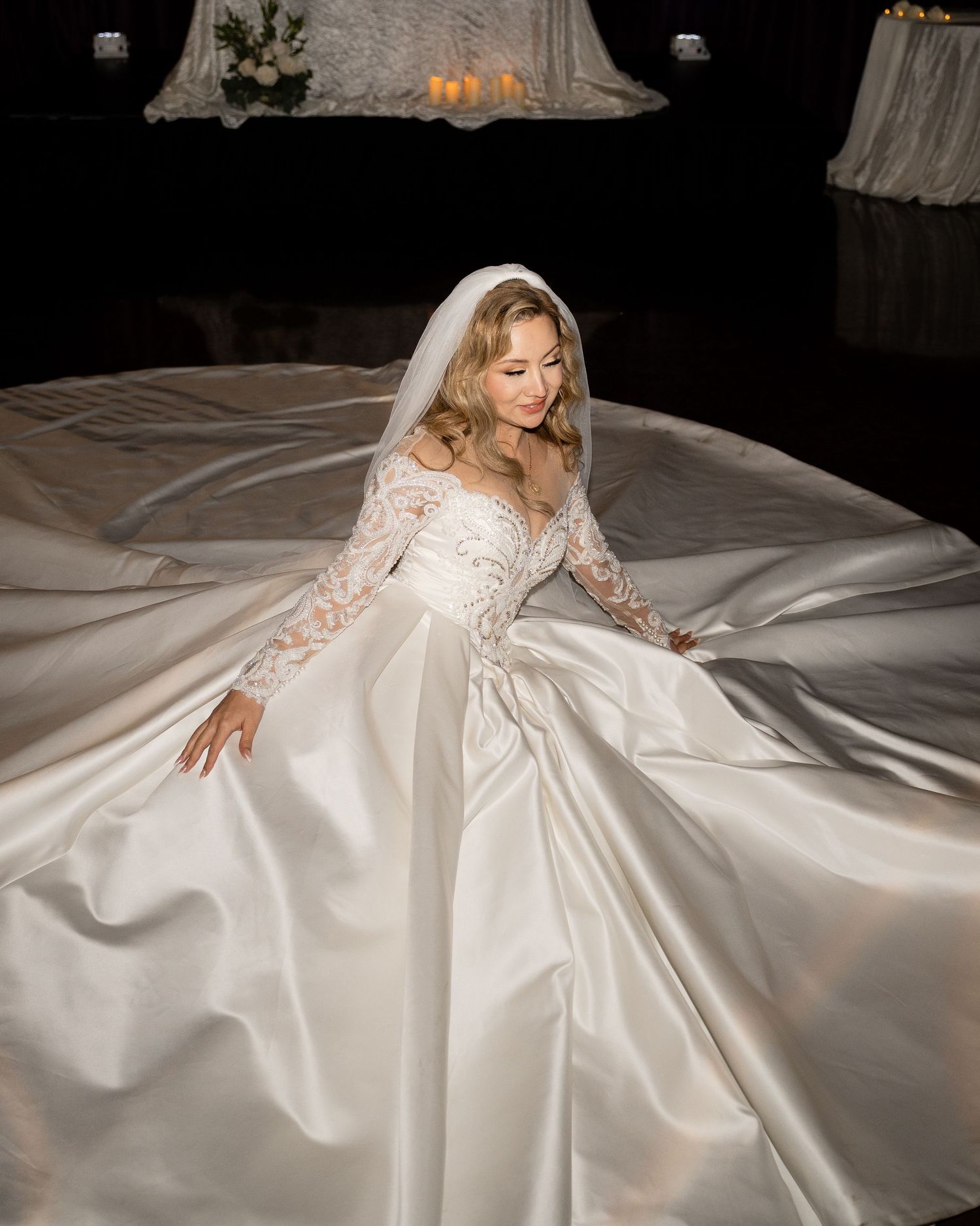 A flowing white wedding gown with lace details spreads dramatically across a light floor.