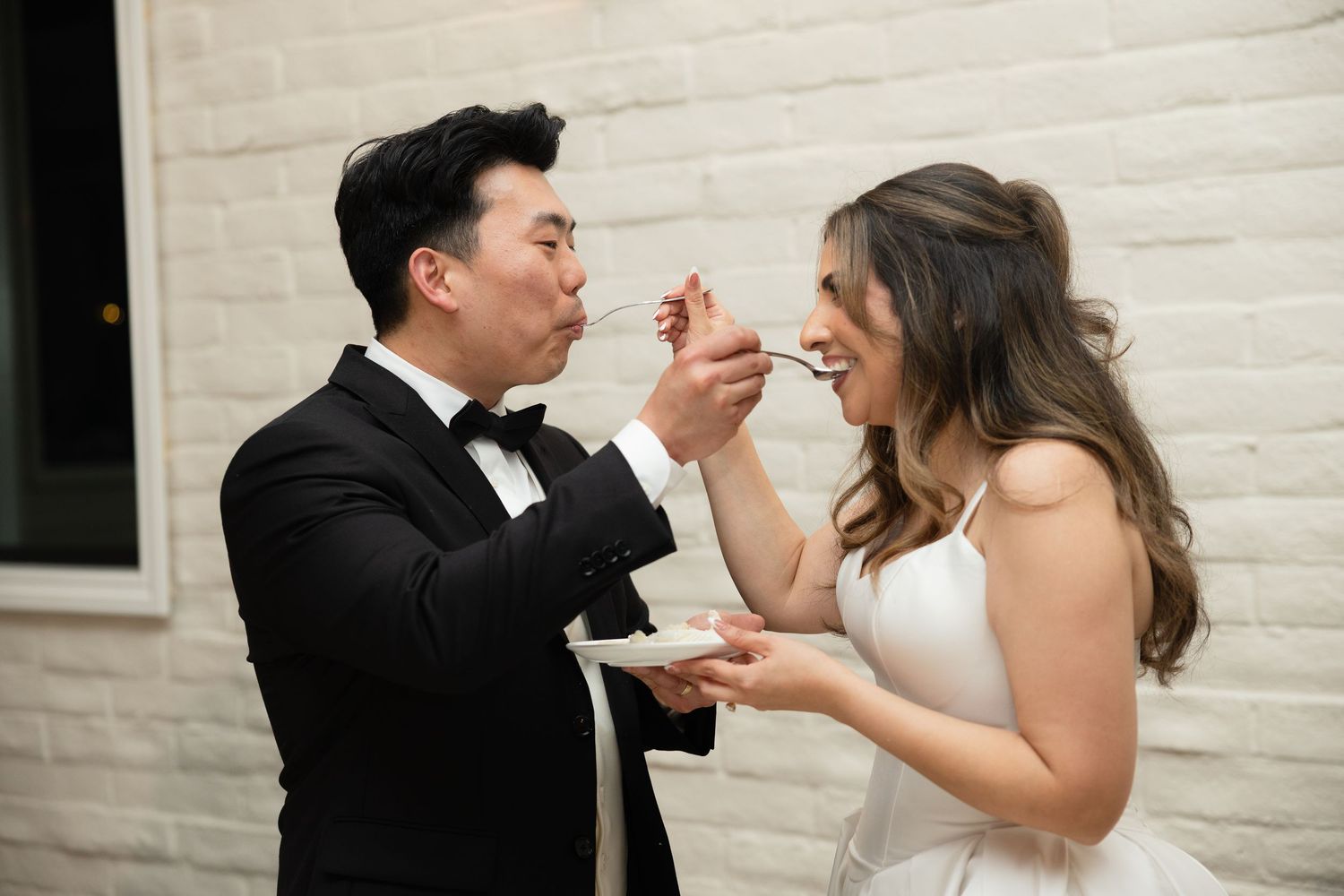 Bride and groom playfully feeding each other cake at wedding reception.