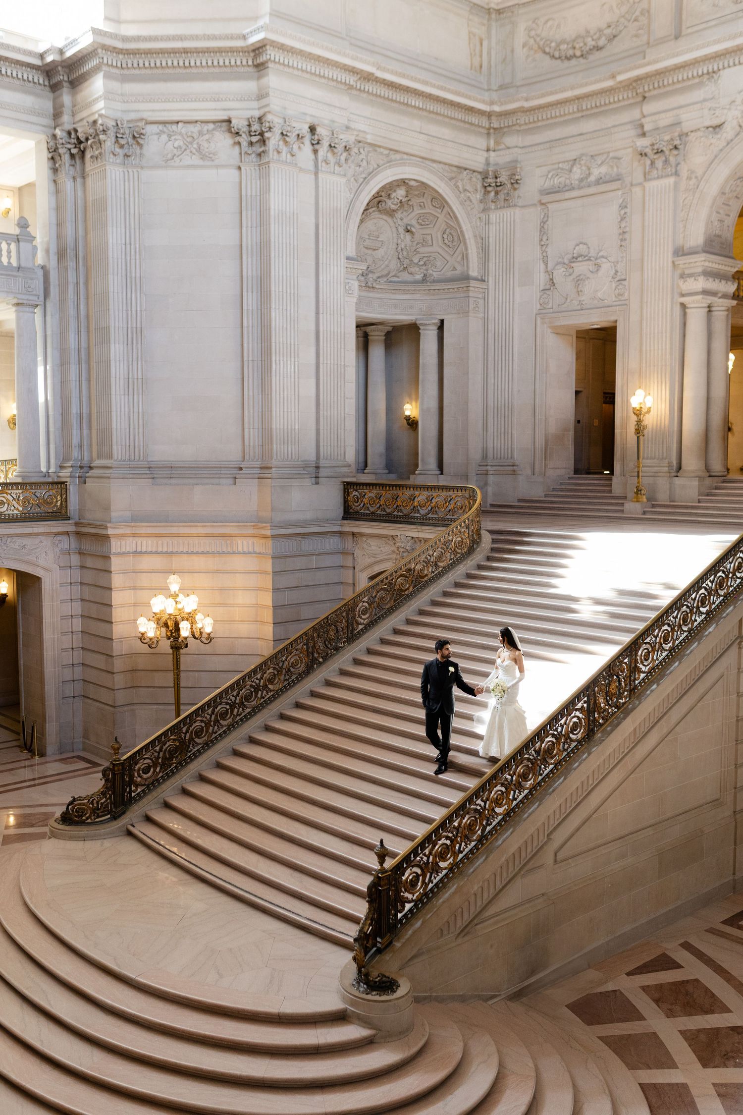 Grand staircase in San Francisco City Hall with ornate marble architecture and elegant lighting fixtures.