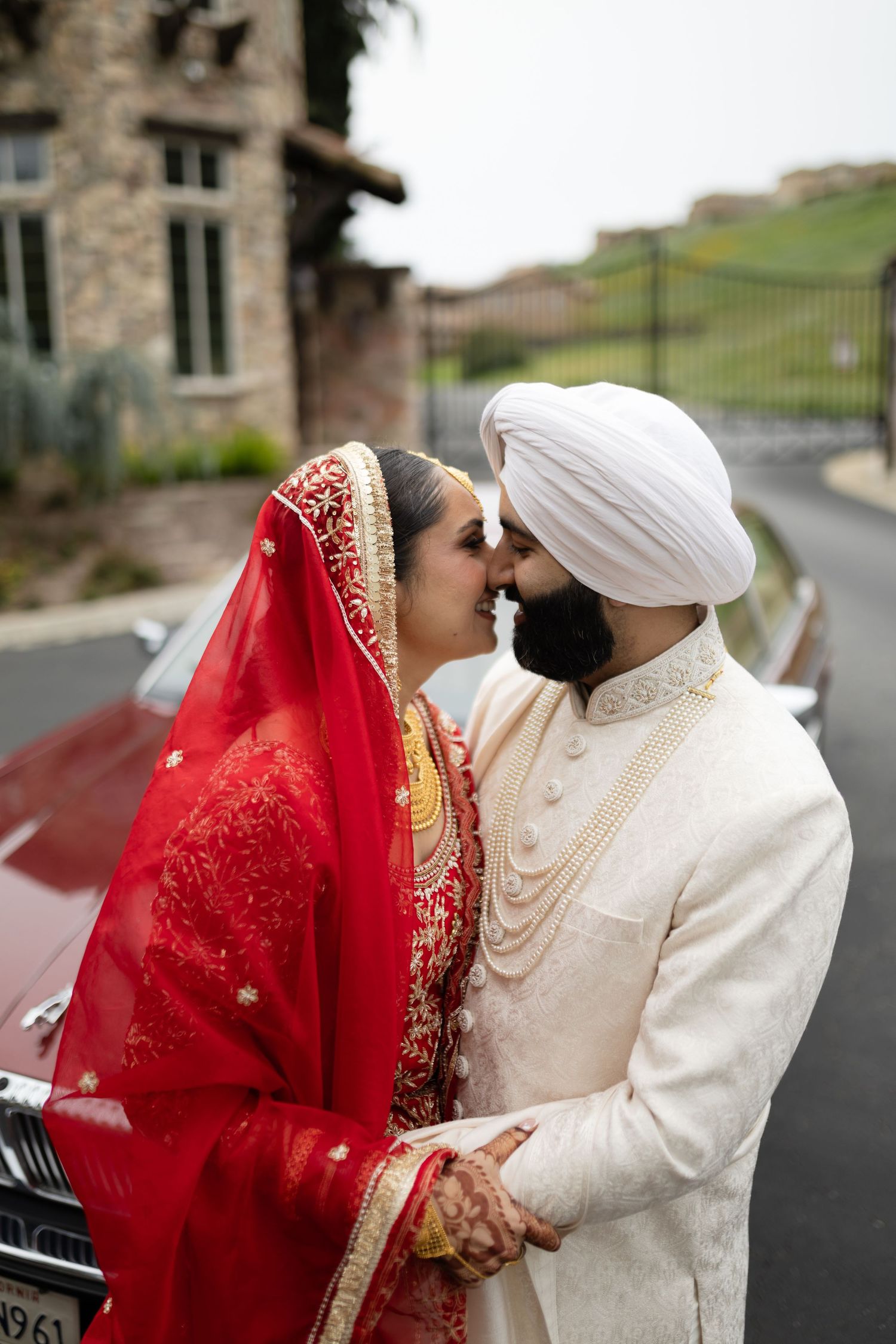 Intimate moment between couple in traditional Indian wedding attire by classic car.