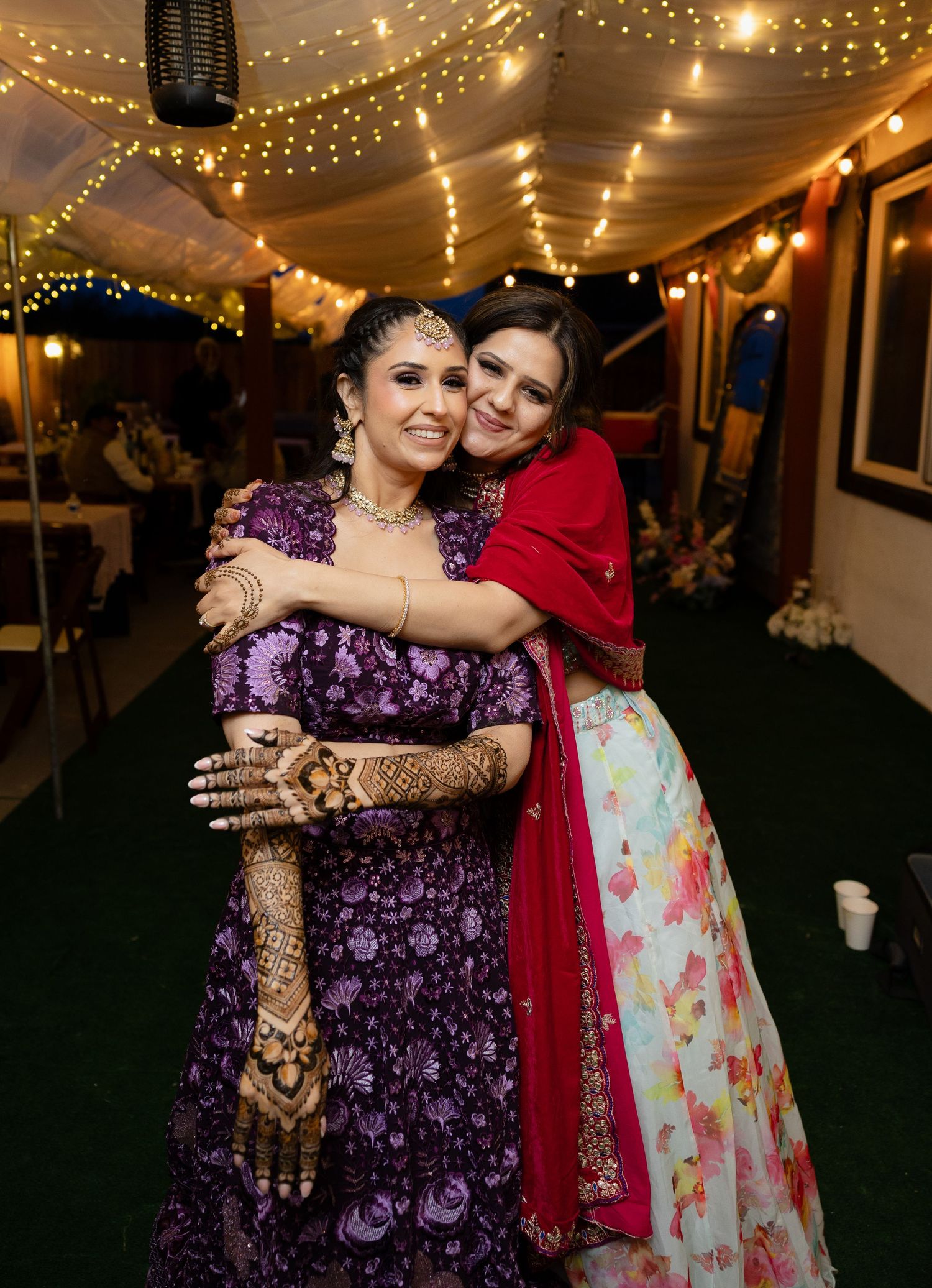 Two people in traditional Indian attire embrace under twinkling lights at a festive celebration.