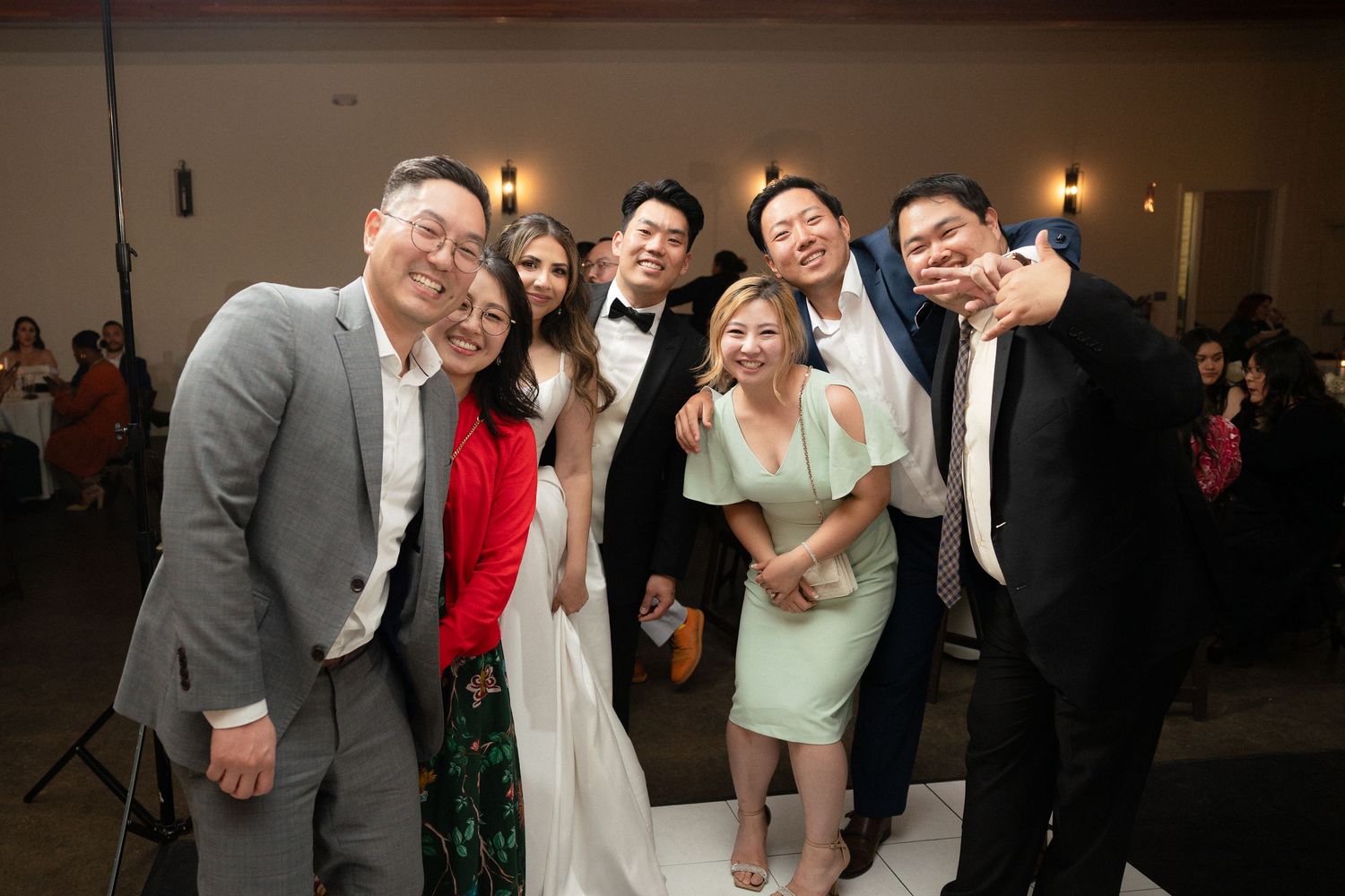 Group of friends posing together at a wedding reception, with bride in white gown and guests in formal attire.