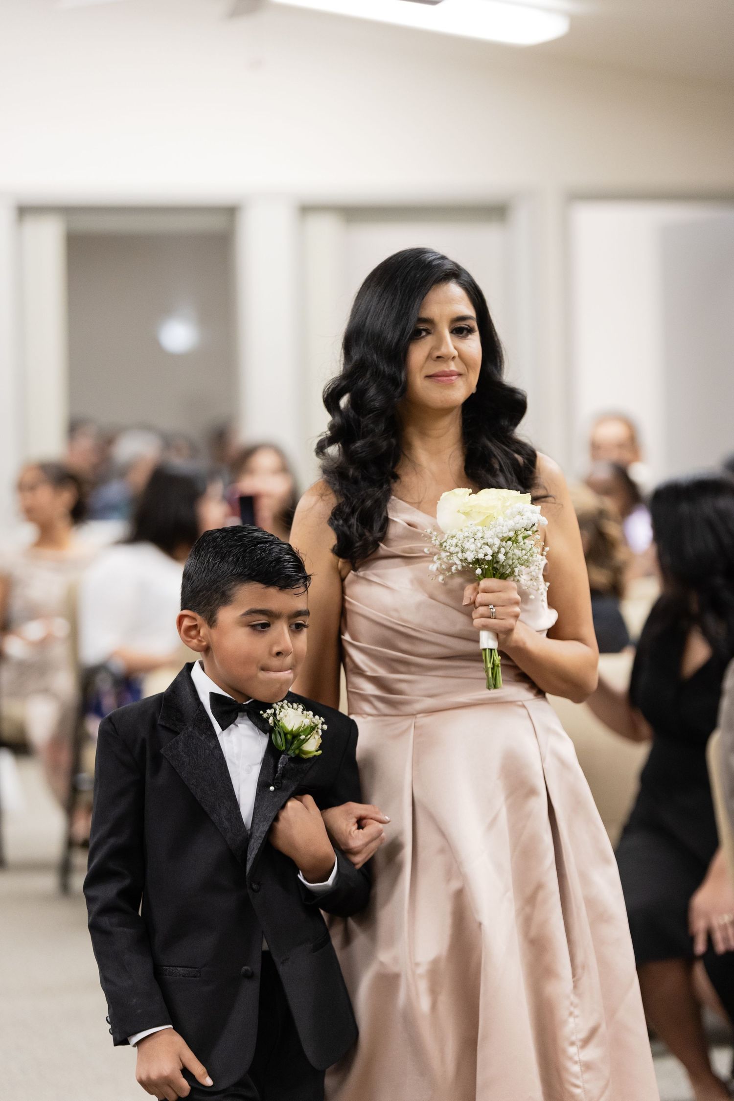 Wedding party members in formal attire walking through an indoor venue.