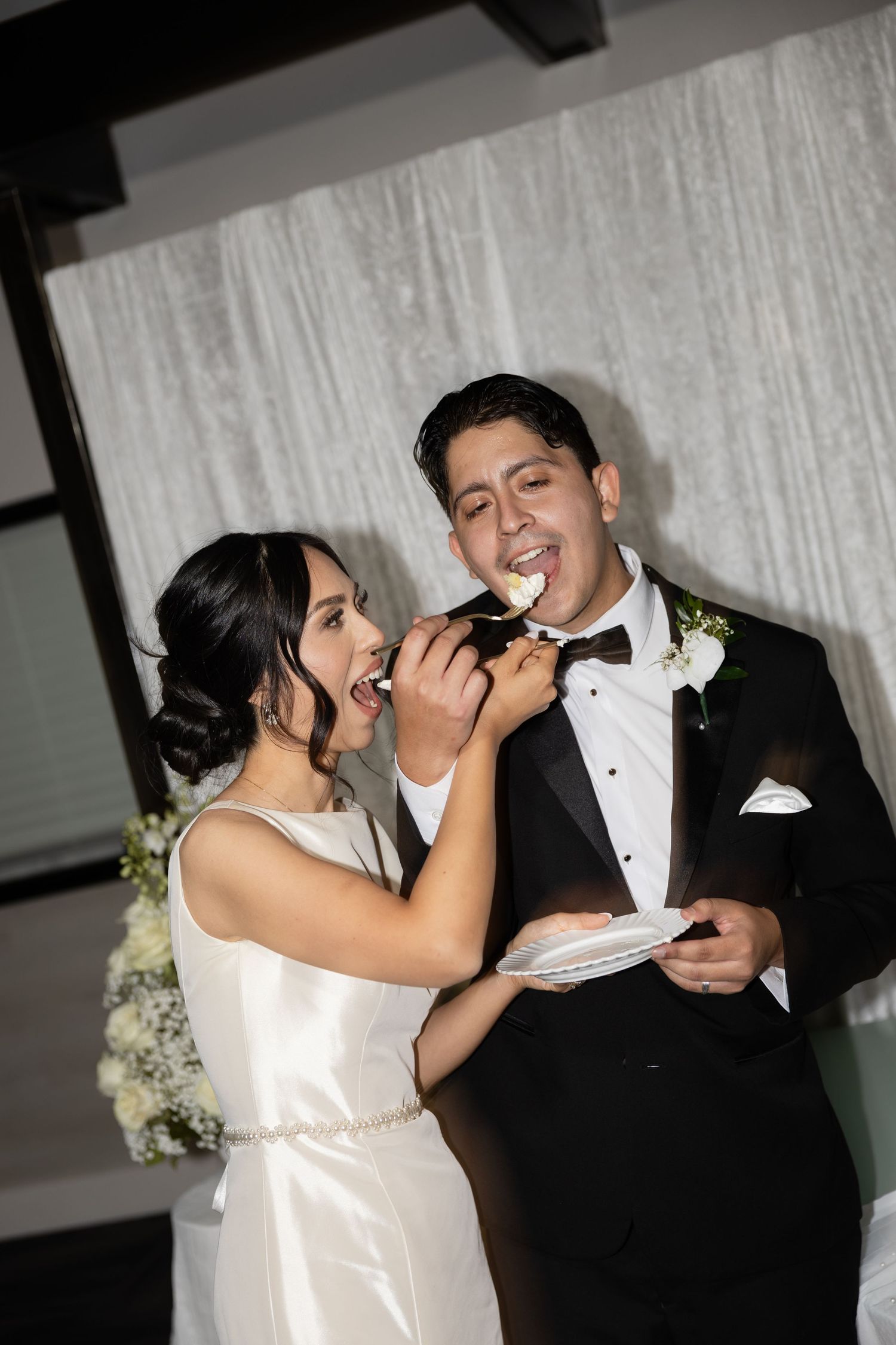 A couple feeds each other wedding cake in a playful cake-cutting tradition.