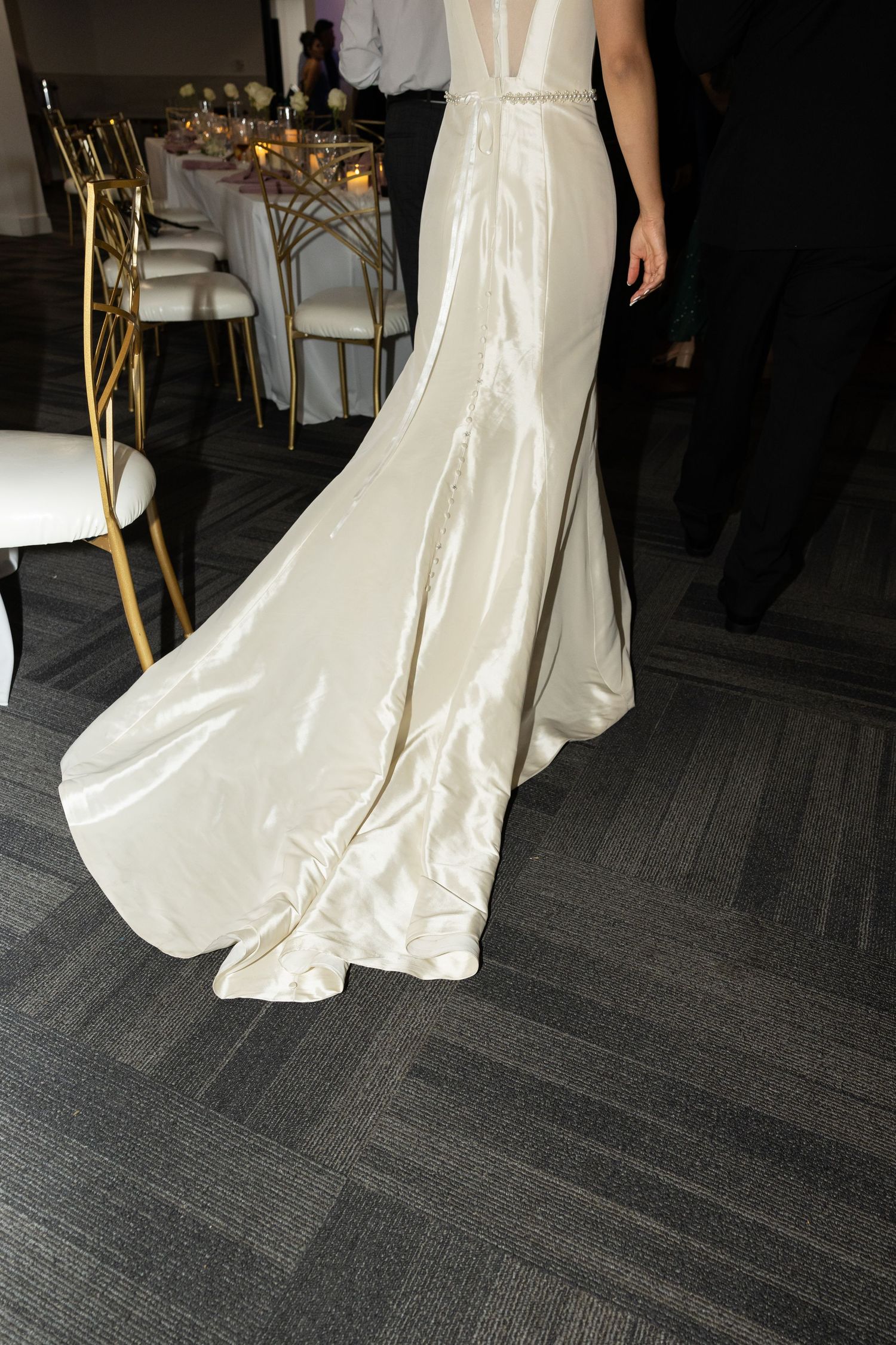 Elegant white wedding dress with long train displayed on dark carpet.