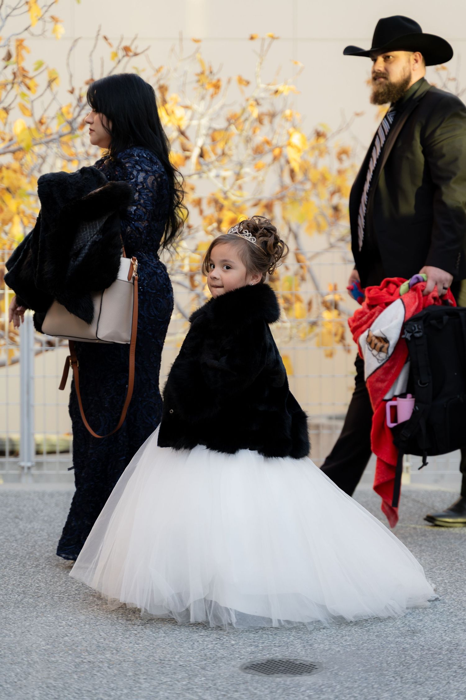 People walking outdoors with a flowing white tulle dress visible among fall foliage.