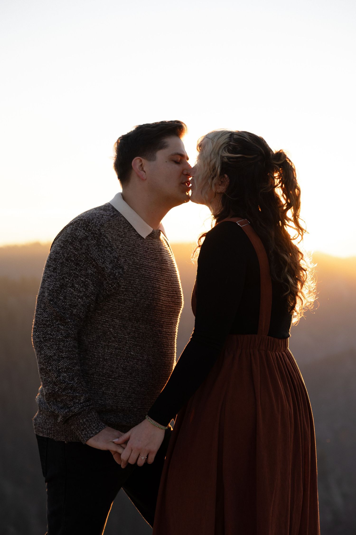 A couple in silhouette shares a tender moment at sunset on a mountain overlook.