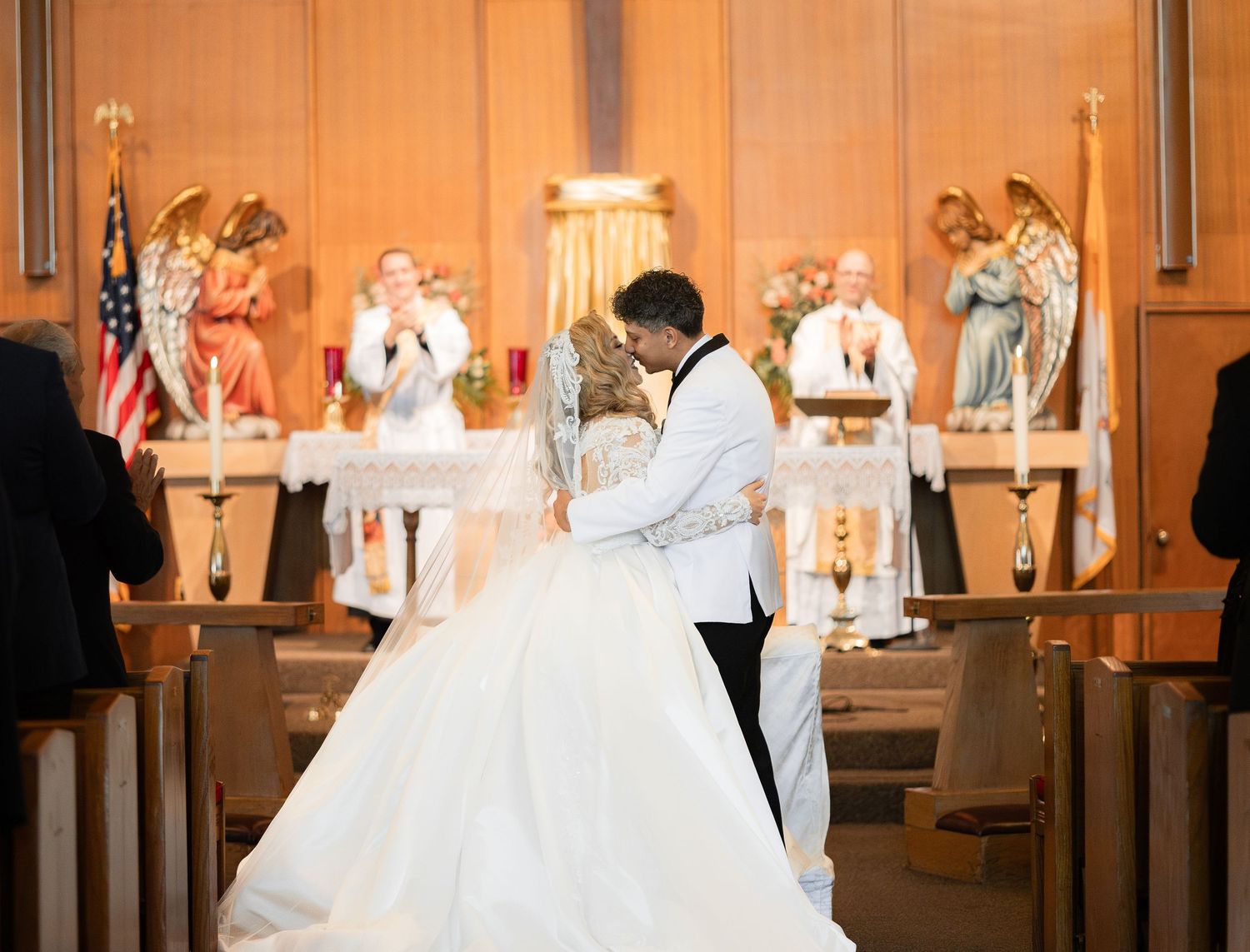 A wedding ceremony in progress at an ornate church altar decorated with American flag and angel statues.