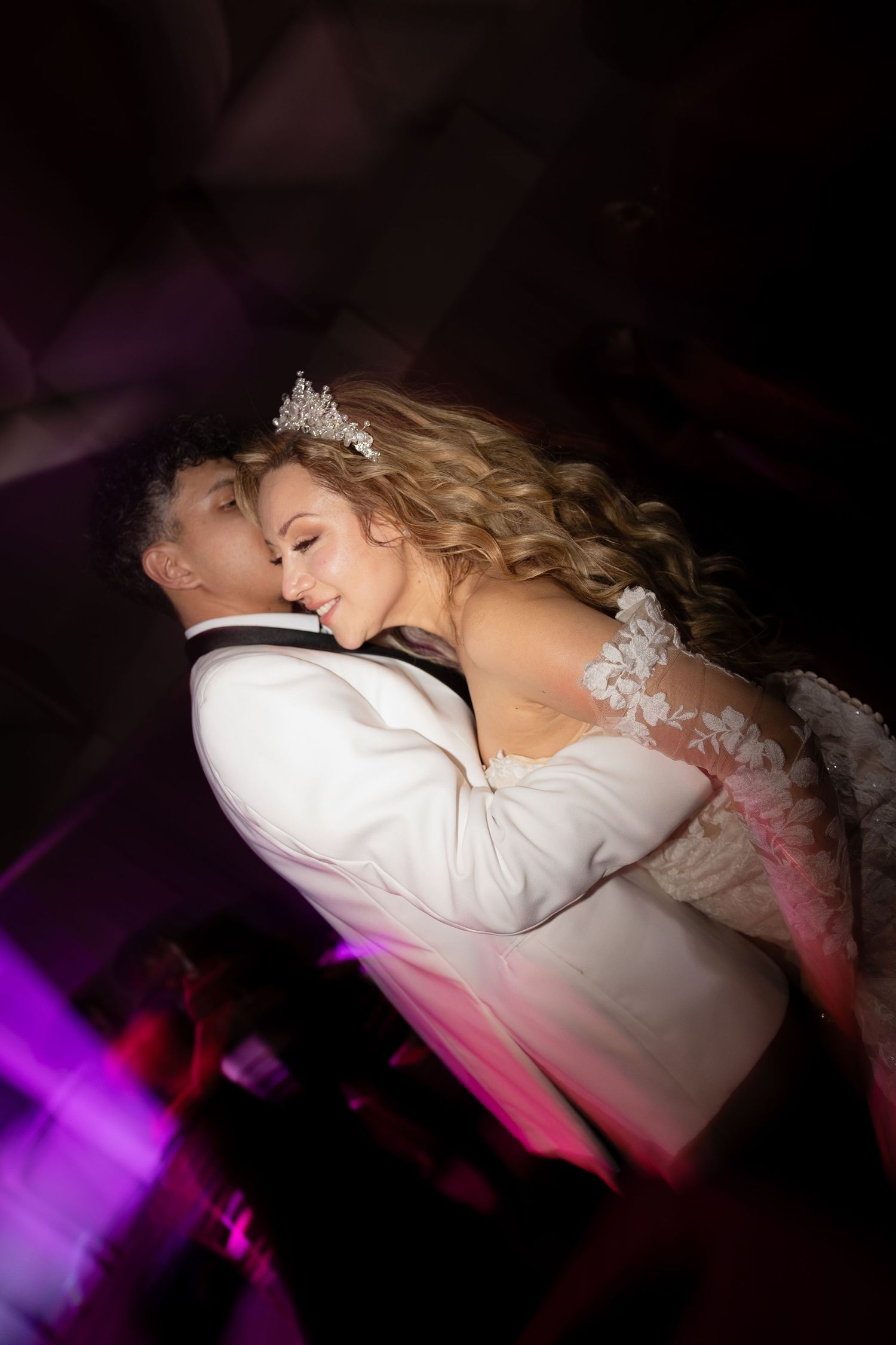 Intimate slow dance moment captured under purple mood lighting at wedding.