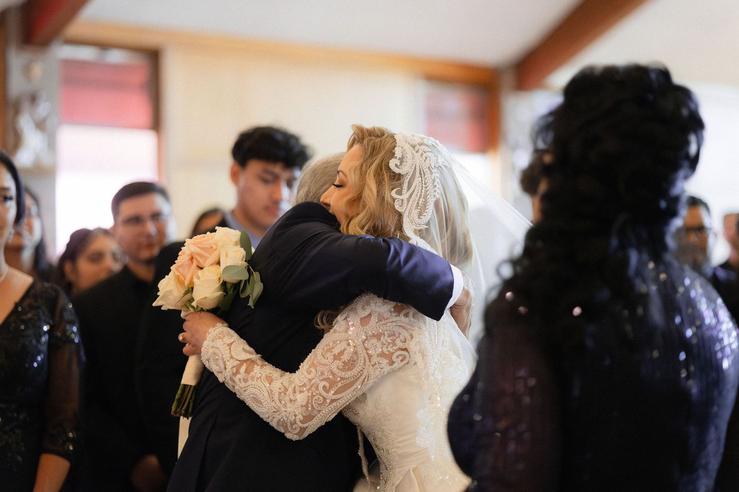 Wedding guests sharing embraces during celebration in church hall.