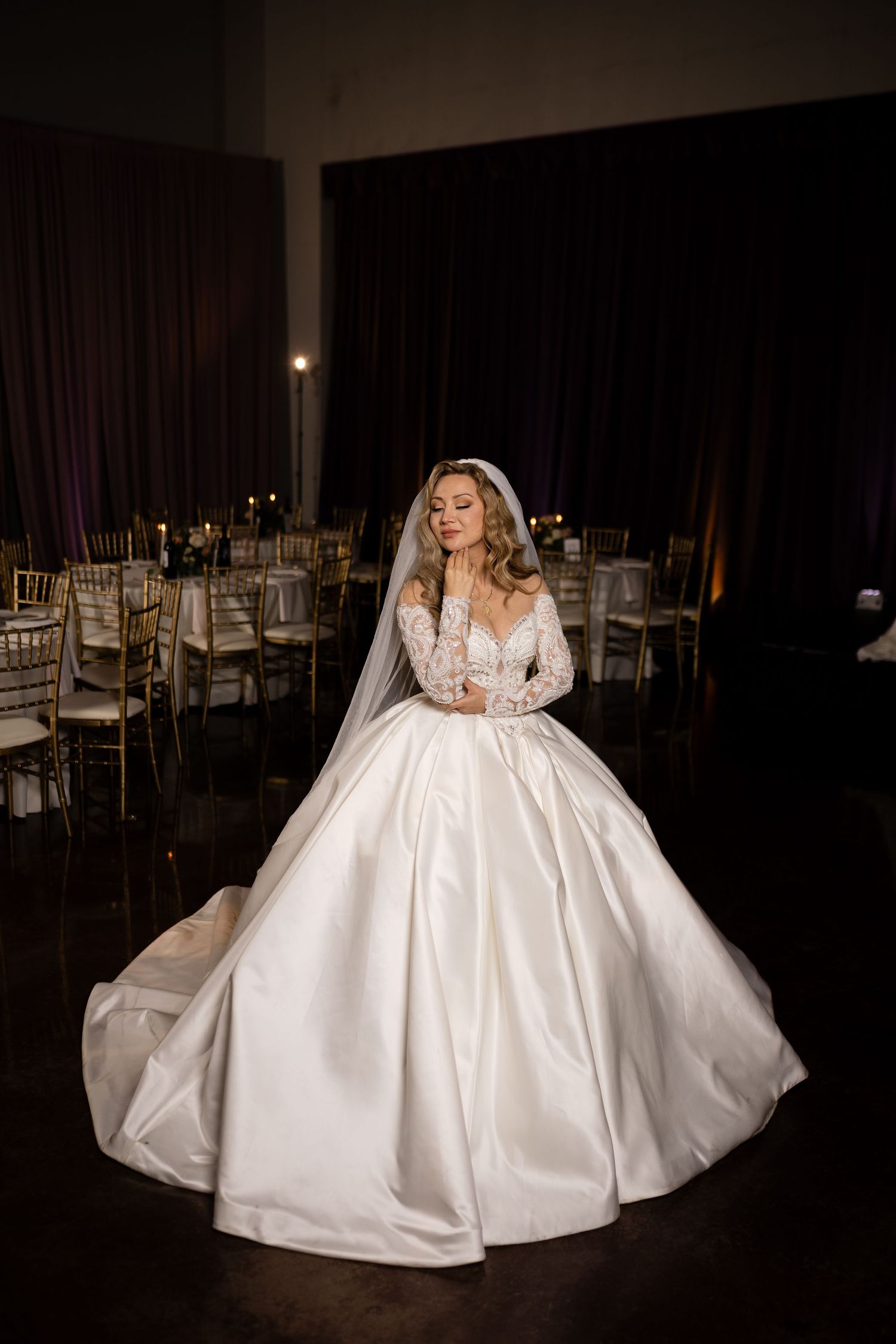 A dramatic bridal portrait in a ballroom featuring a luxurious white wedding gown with long sleeves.