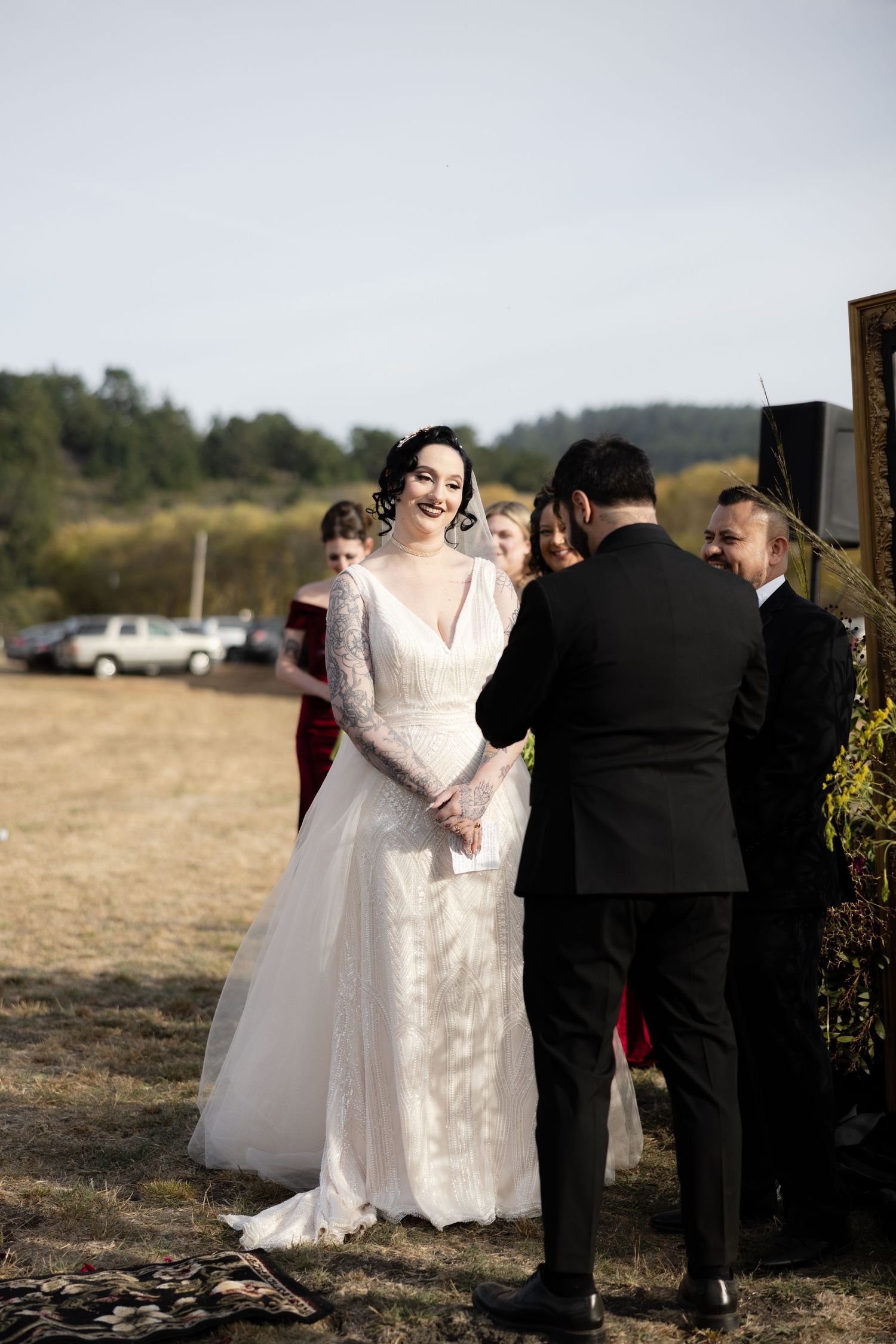 Wedding party members stand together near decorative wooden arch during outdoor ceremony.