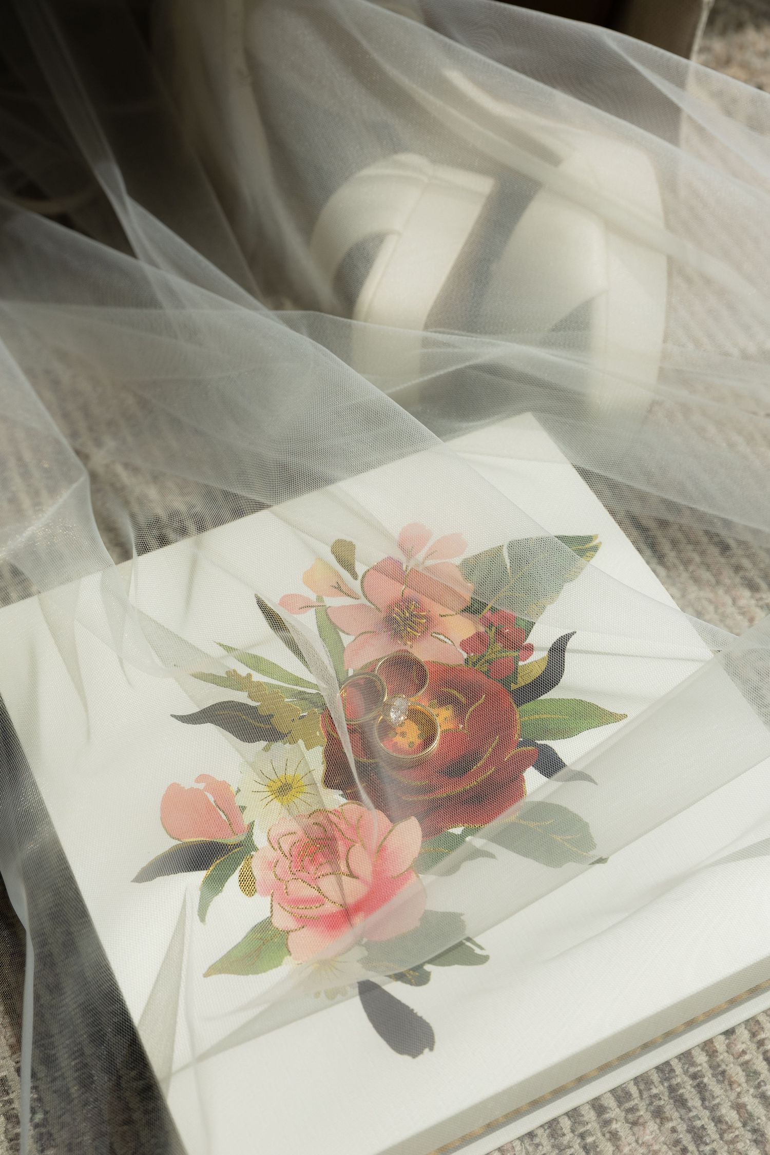 Floral wedding gift box with pink roses under sheer white veil on textured surface.