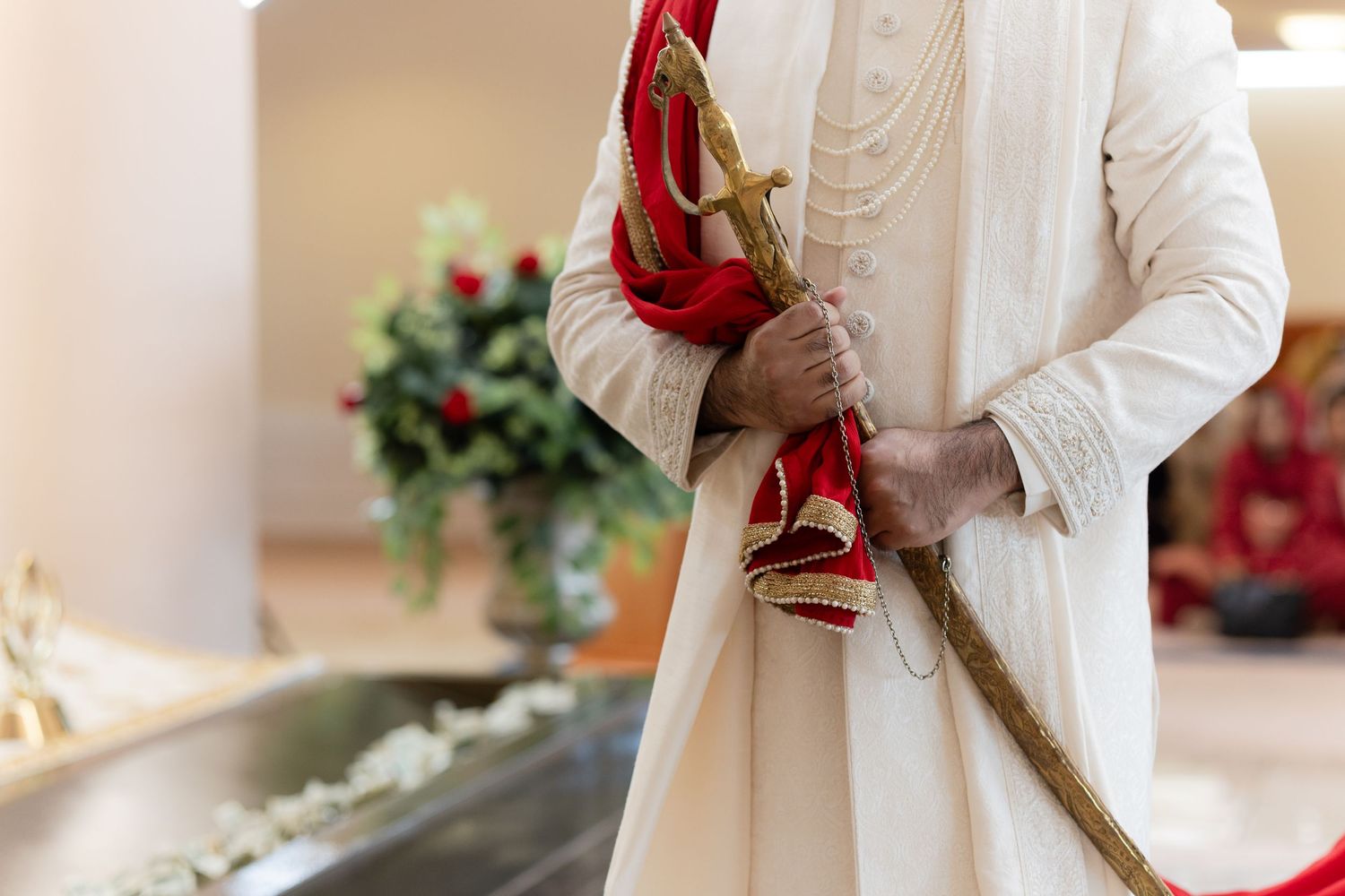A person in white clothing holds red high heel shoes and rope against a light background with floral decorations.