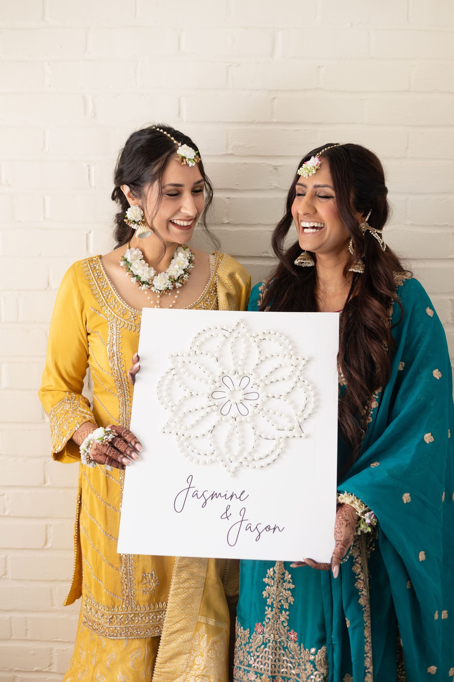 Two people in traditional Indian attire holding decorative name cards while laughing together.
