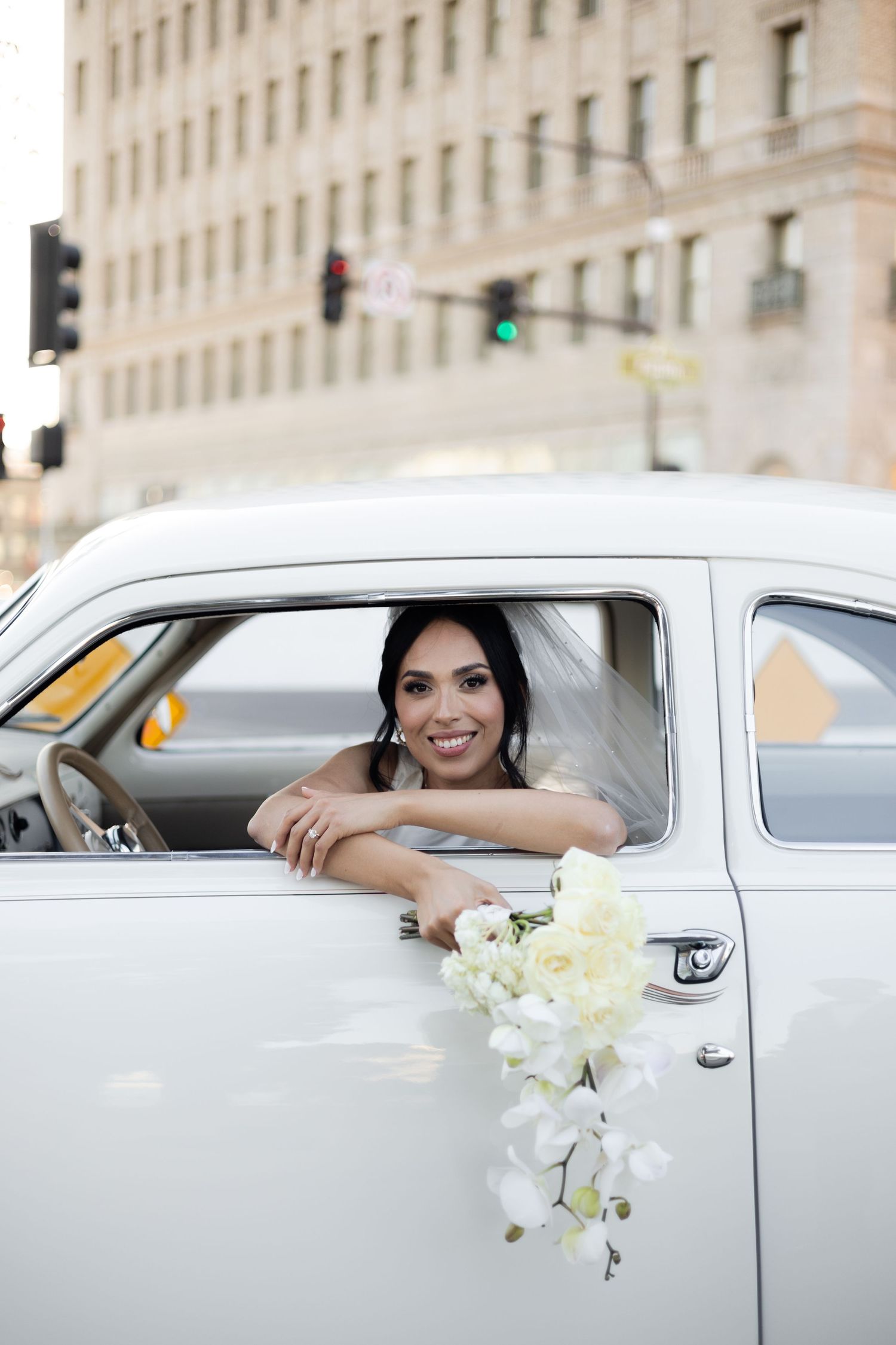 White vintage car with floral decorations parked by historic building during wedding photoshoot.
