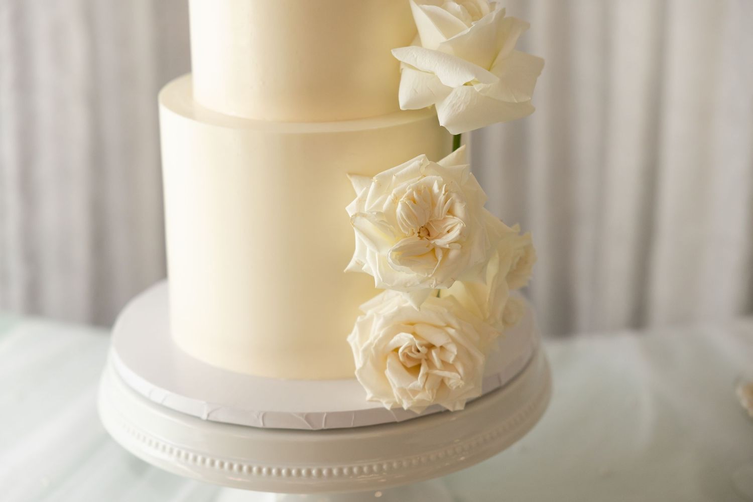 Classic white wedding cake decorated with delicate flowers and pearls on a simple white stand.