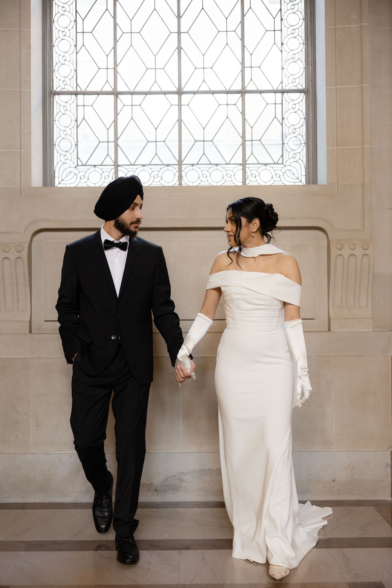 A couple walking and posing in an elegant hallway with geometric windows.