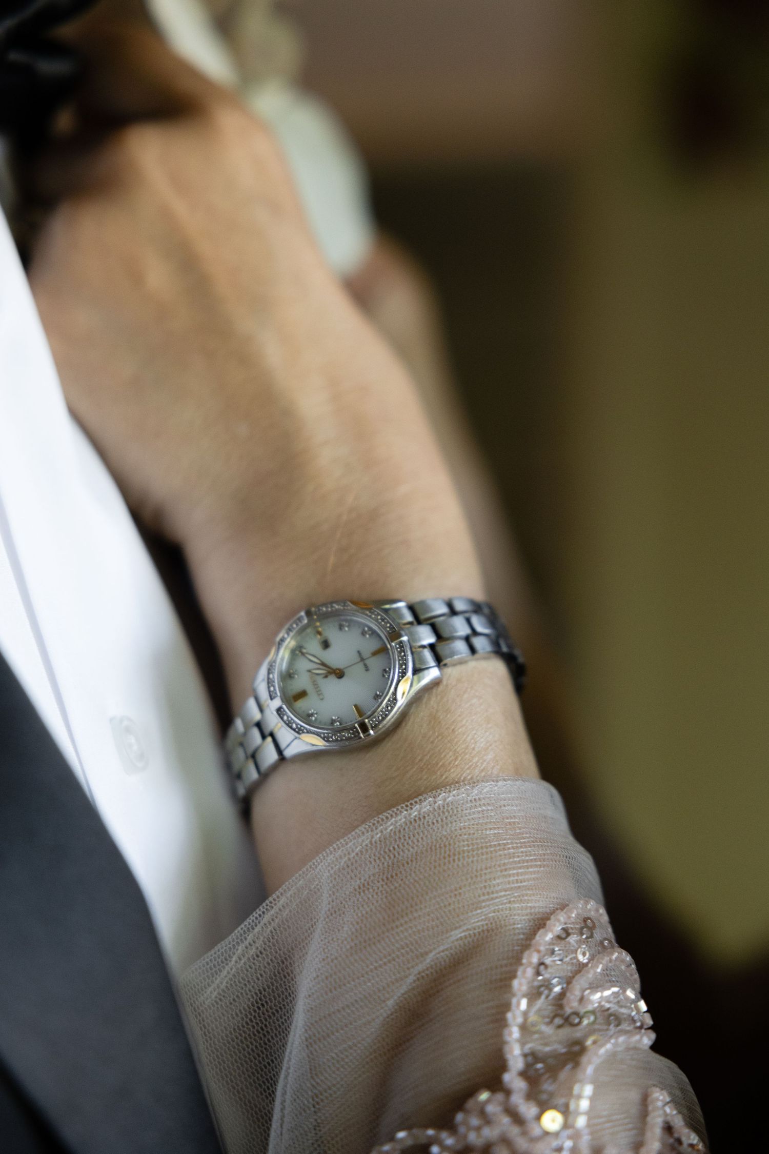 Close-up of an elegant wrist watch and lace detail on formal attire.