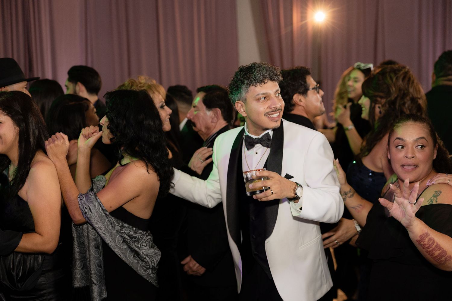 Guests dancing and celebrating at an elegant wedding reception with pink lighting.
