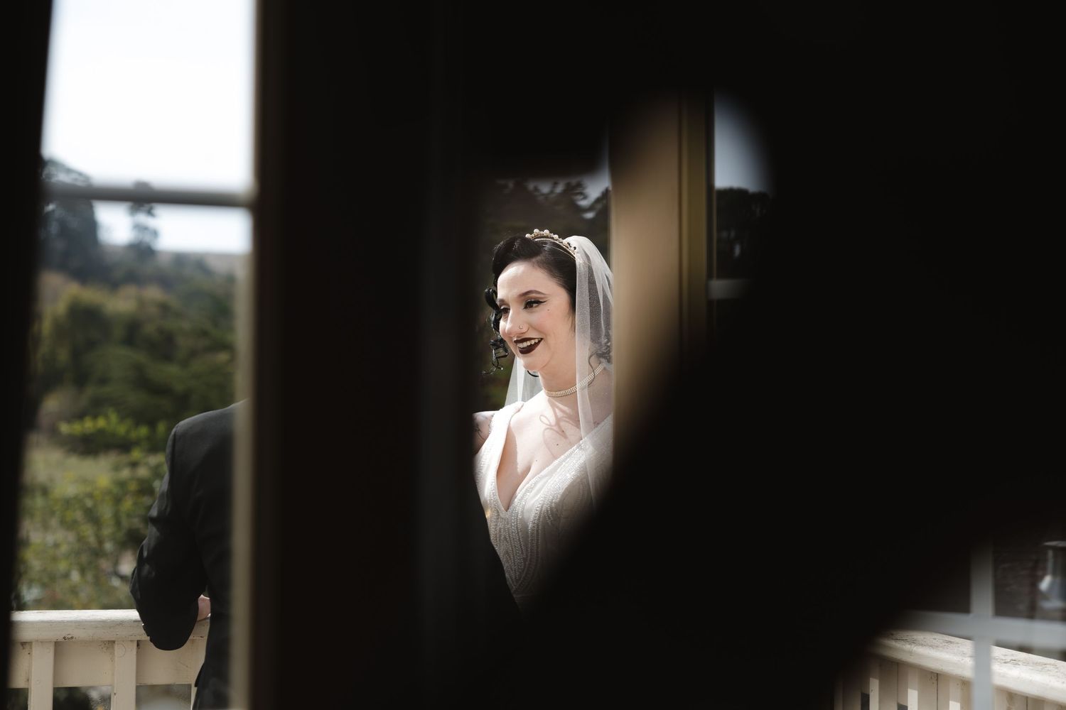 Artistic framed shot through doorway of bride in classic white gown and veil.