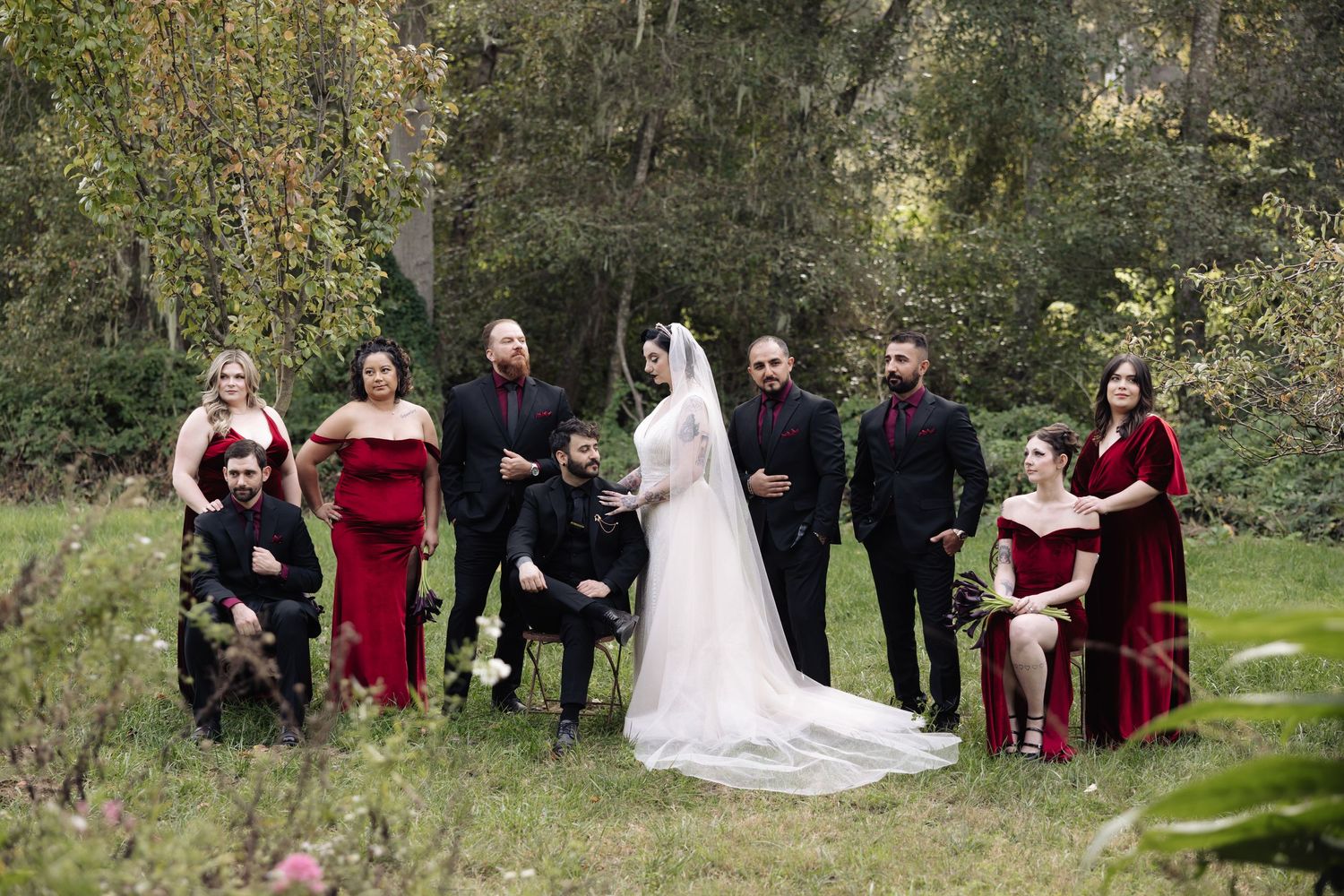 Wedding party gathered outdoors in autumn setting with burgundy and black attire.