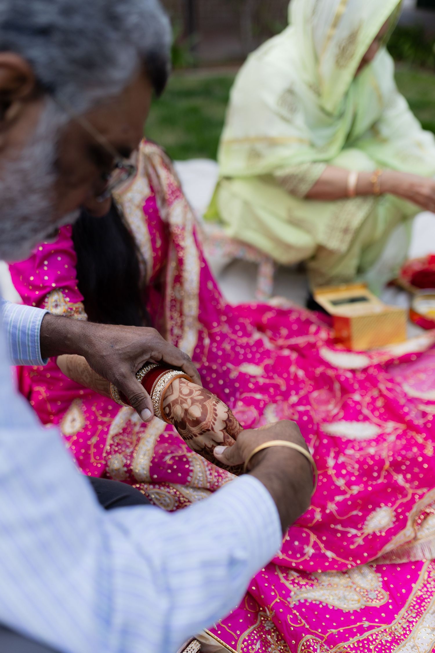 Hands adorned with traditional henna designs are shown against a bright pink and white fabric background.
