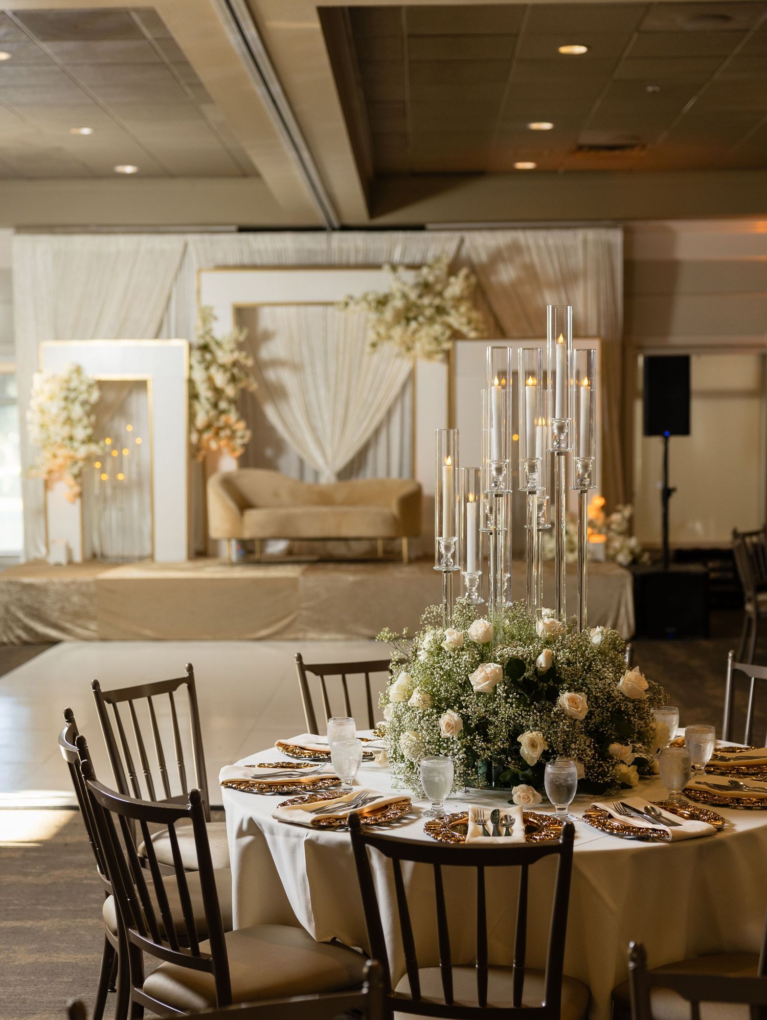 Elegant wedding reception table setting with tall candles, floral centerpieces and draped backdrop decor.