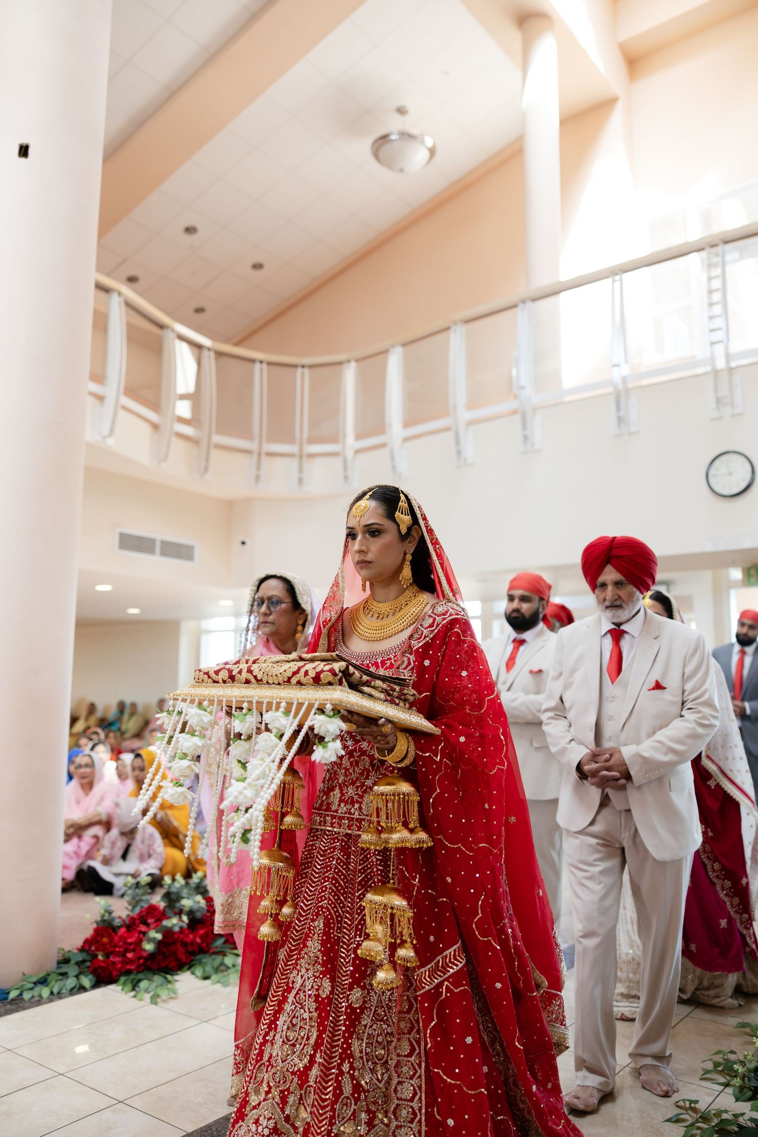 Traditional Sikh wedding ceremony taking place in a bright indoor venue with white pillars and decorative elements.