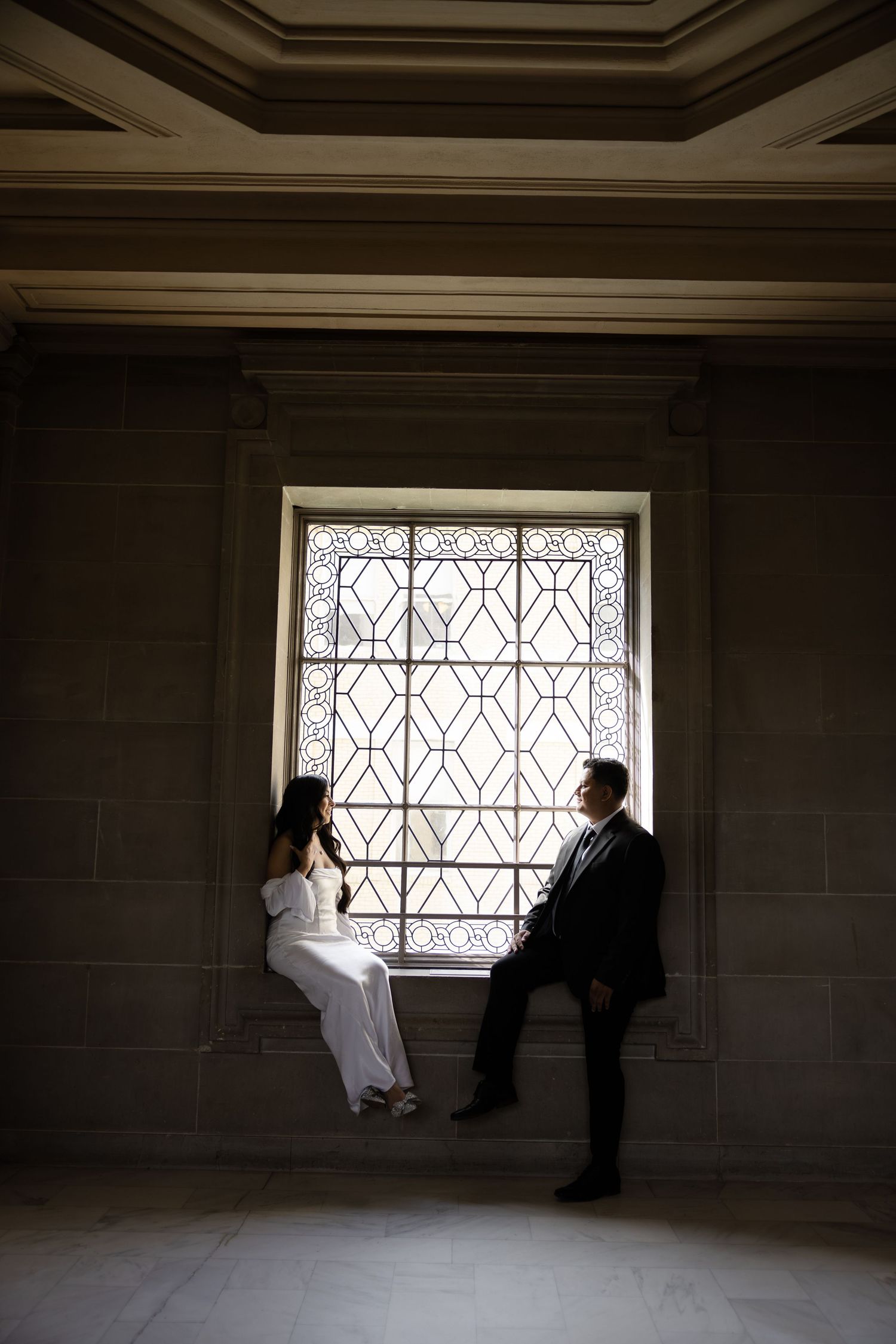 Silhouettes against geometric patterned windows in a dimly lit interior space.