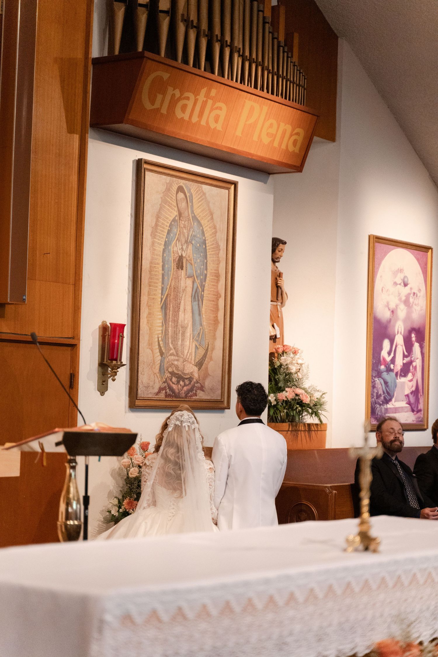 Church altar with religious artwork and wooden organ pipes during wedding ceremony.