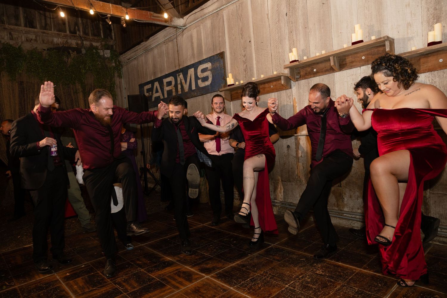 Group dance performance unfolds on wooden floor at barn wedding venue.