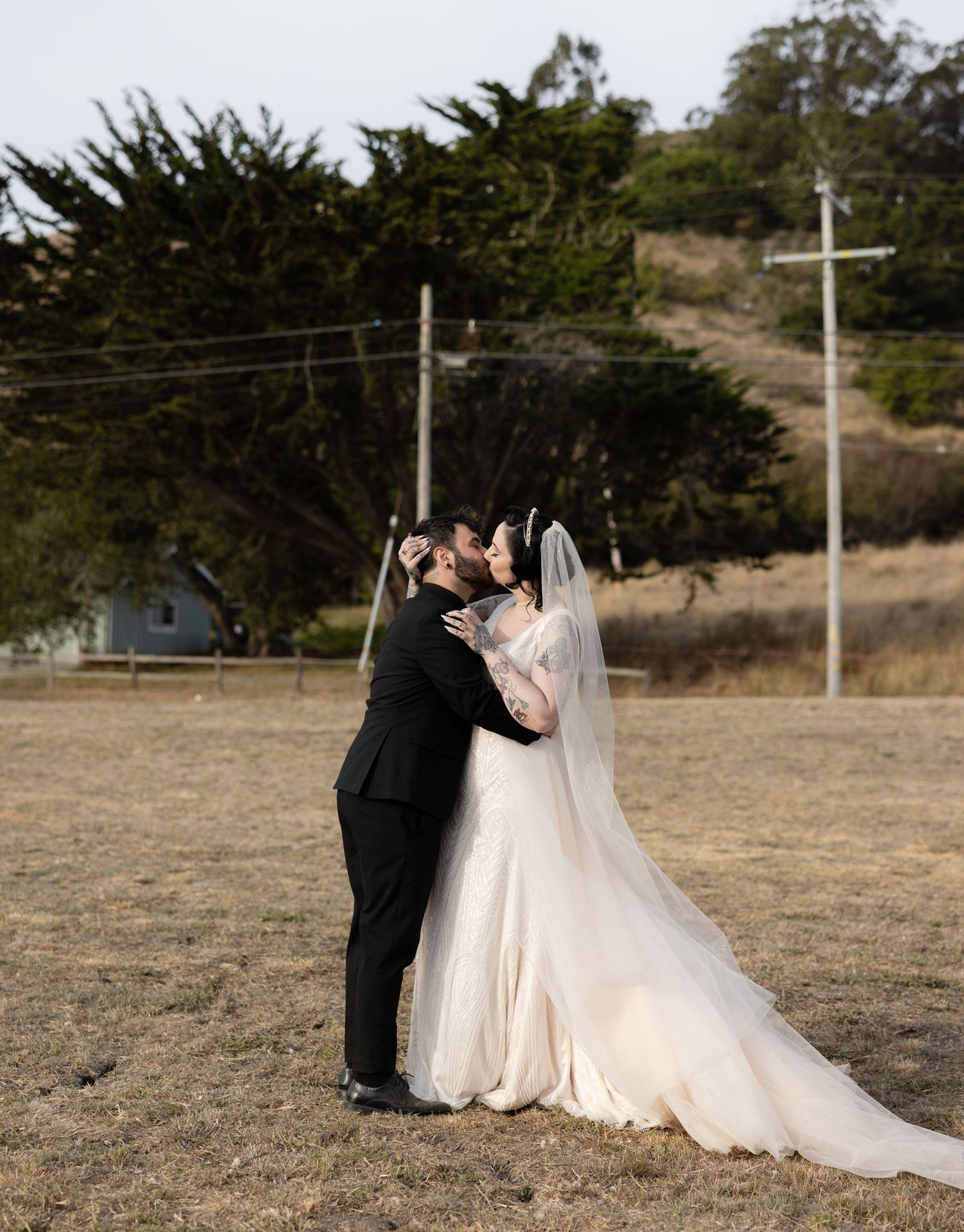 Wedding couple sharing intimate moment in rustic outdoor setting with power lines in background.