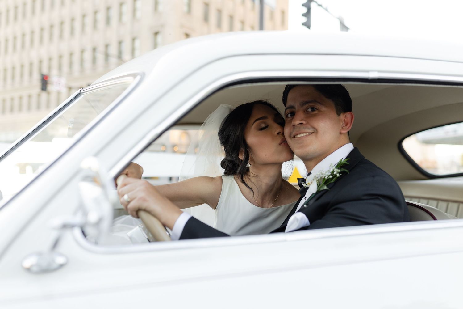 Newlyweds share joyful moments inside a classic white vintage car.