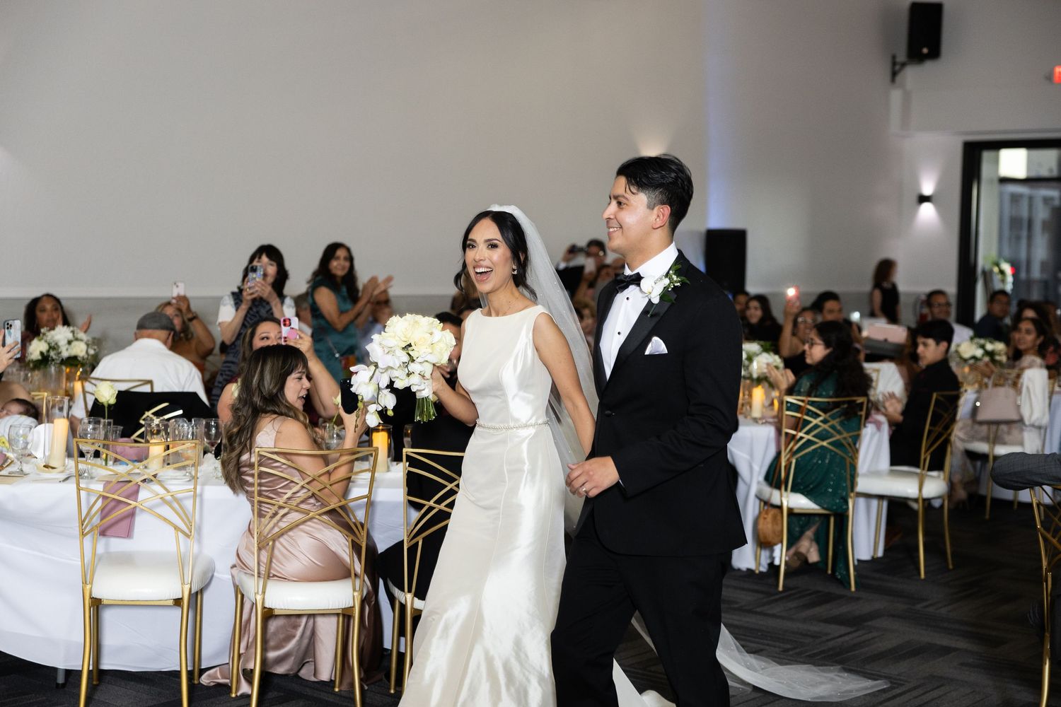 Wedding reception guests enjoy a lively celebration in an elegant white-decorated venue.
