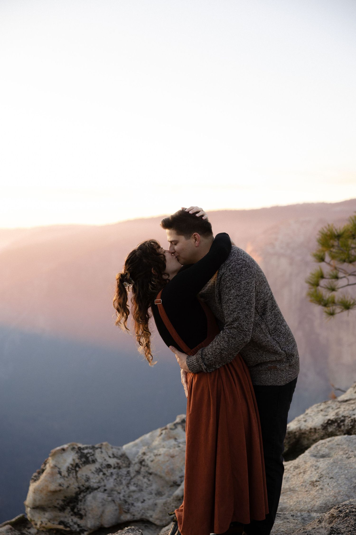 A romantic scene unfolds on a mountain cliff edge during sunset.