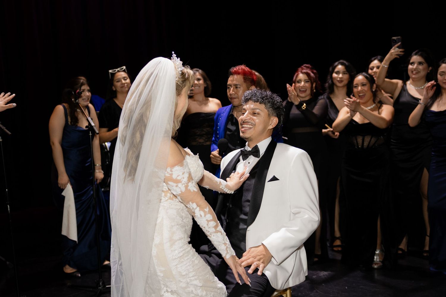 A couple shares a dance at their wedding reception while guests in formal attire cheer them on.