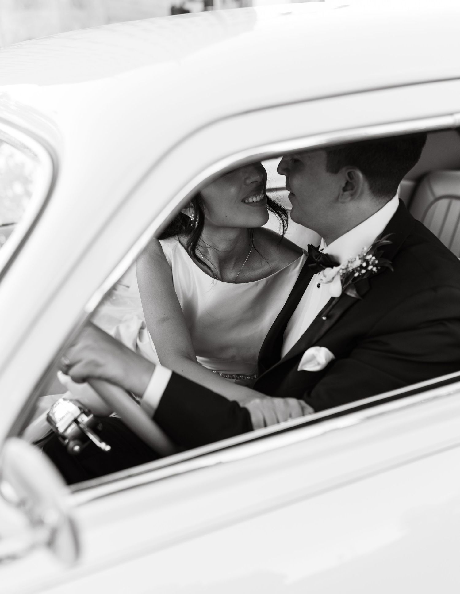 Black and white photo of a couple sharing an intimate moment in a vintage car.