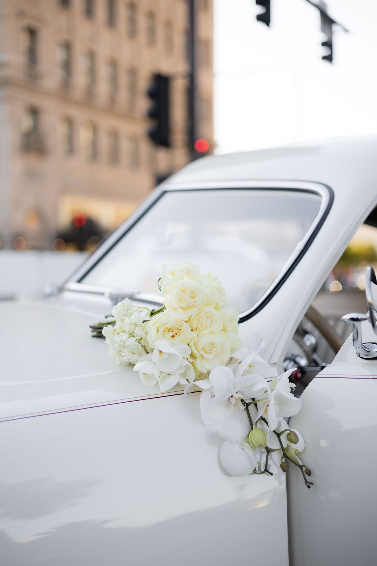 White vintage car decorated with cream roses and floral arrangements for wedding celebration.