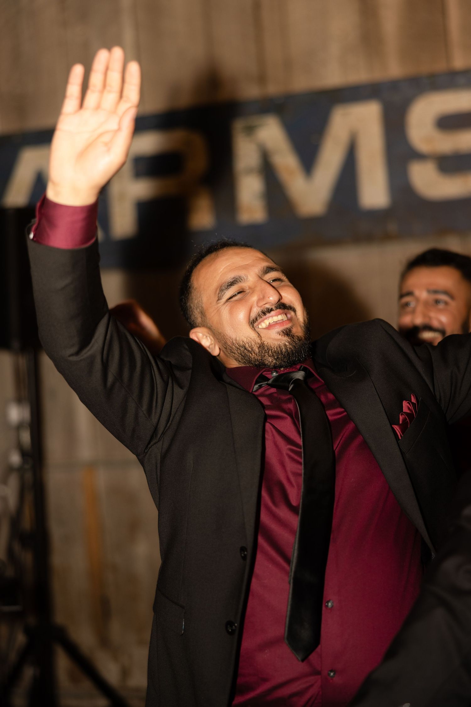 Wedding guest raising hands joyfully during celebration in dark venue.